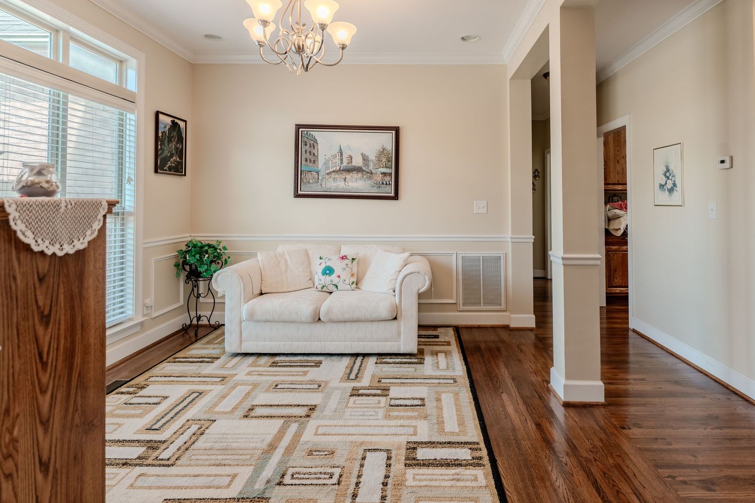 Elegant living room with hardwood floors featuring geometric inlay patterns and a crystal chandelier overhead.