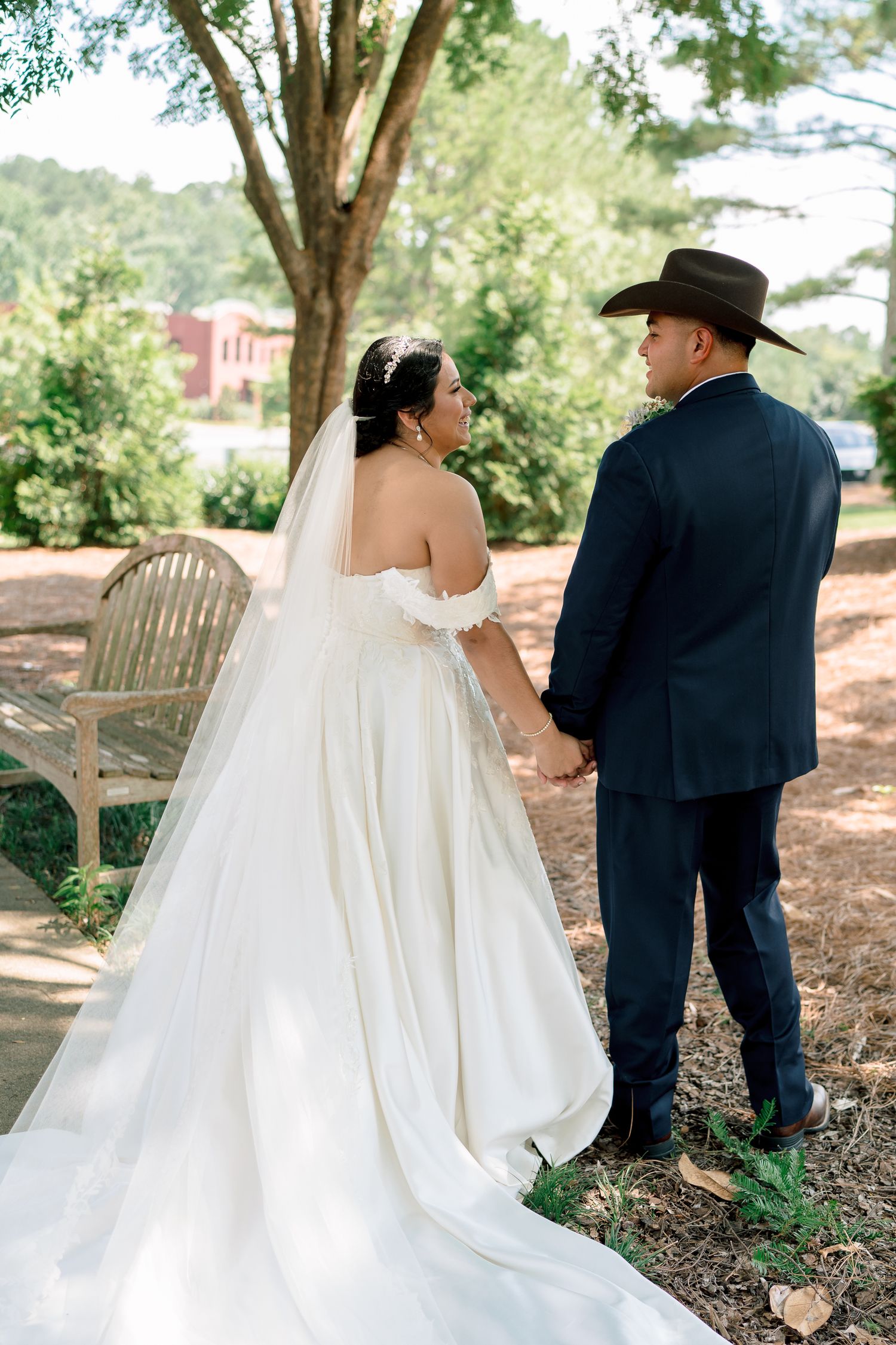 Romantic wedding moment captured in nature as couple stands together on wooded path near rustic bench.