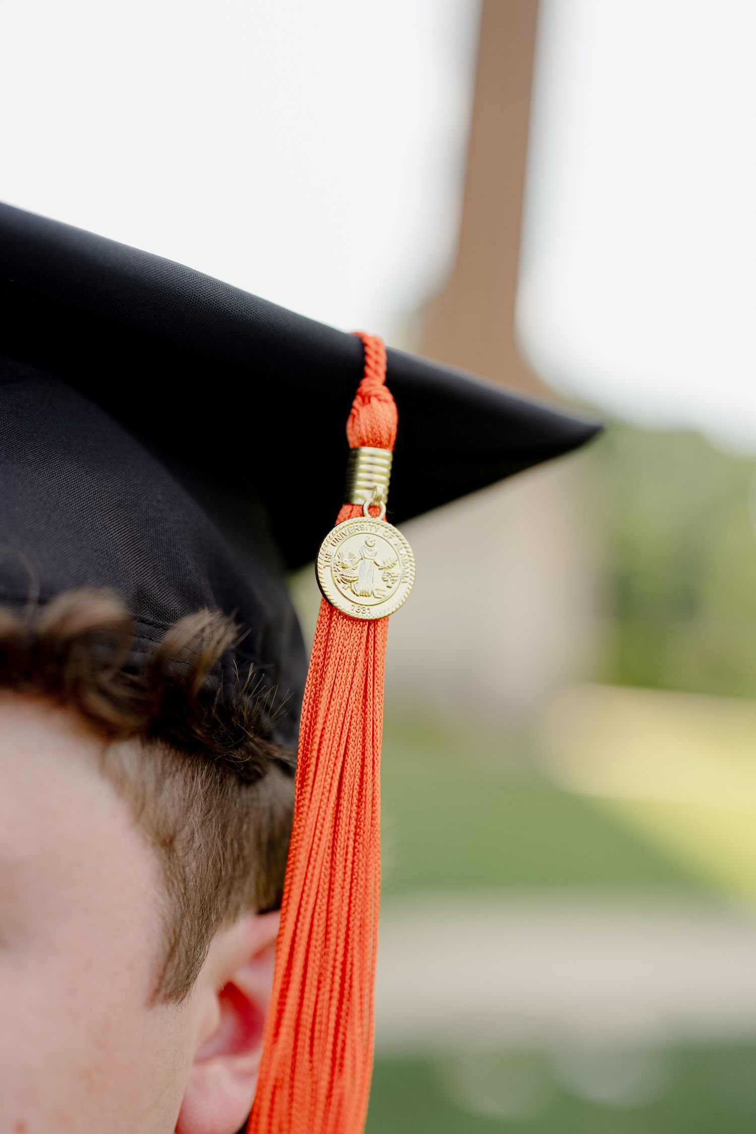 Close-up of a black graduation cap with an orange tassel and gold medallion worn by a graduate.