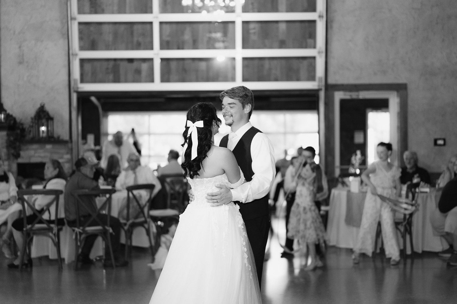 Bride and groom share romantic first dance in black and white photo inside elegant wedding reception.