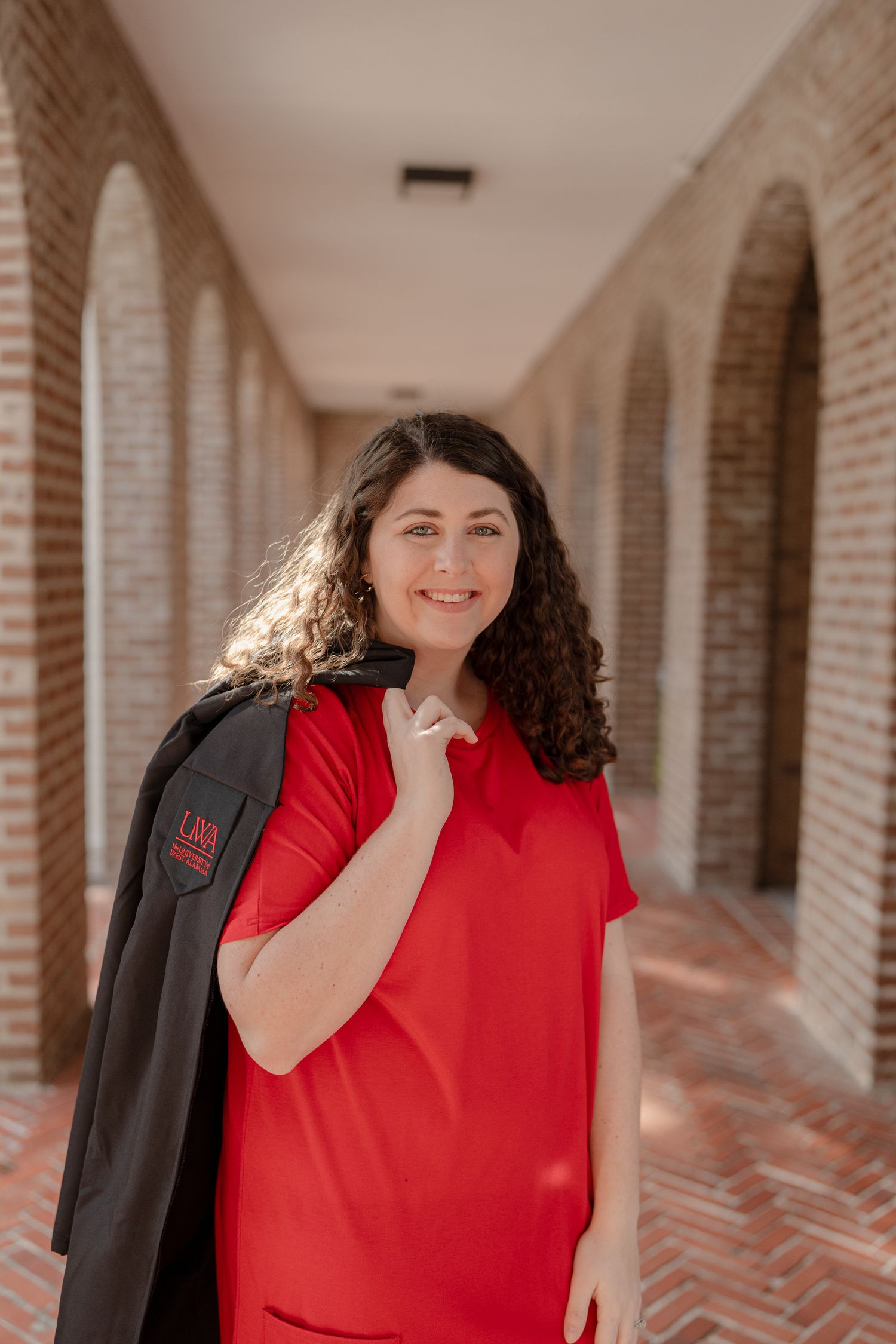Person in a bright red top smiles while standing in an arched brick hallway with natural lighting.
