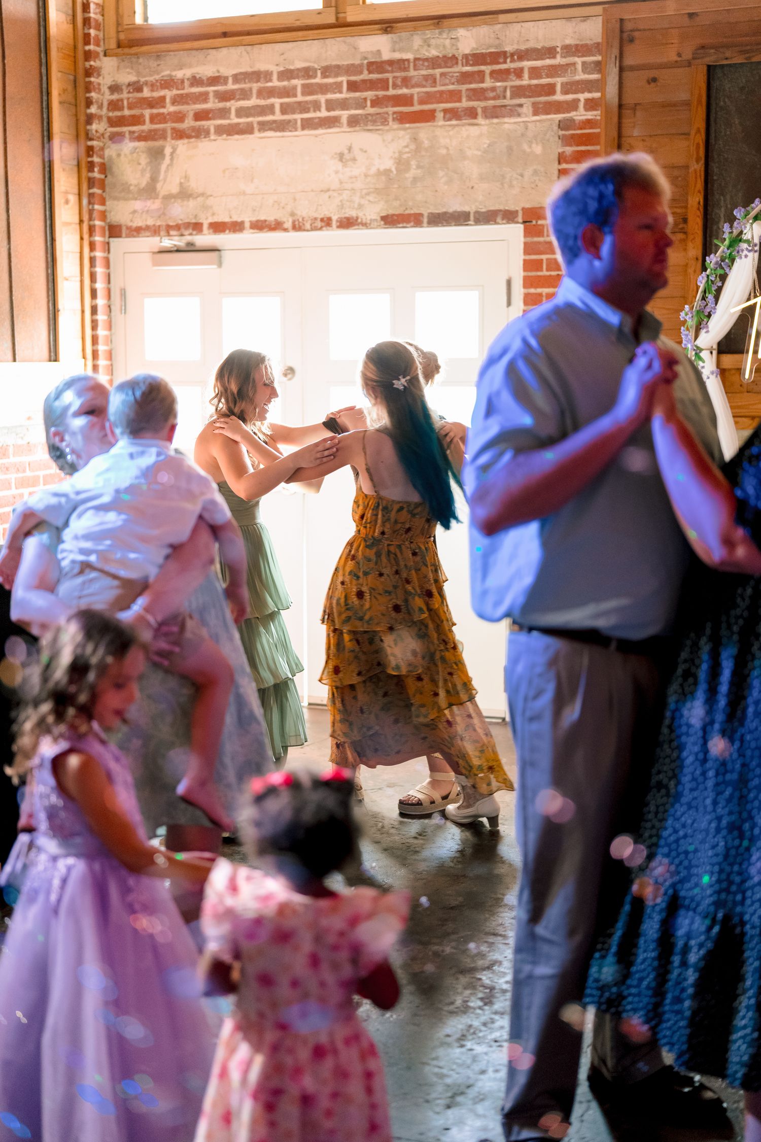 Guests dancing at a rustic wedding reception in a brick venue, with children and adults celebrating together.