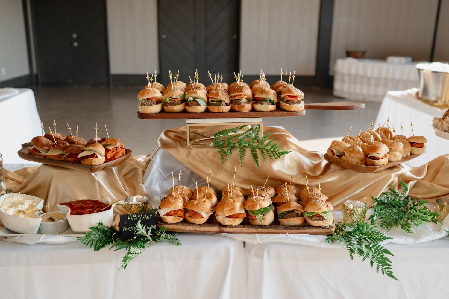 Elegant display of appetizers and sliders on wooden boards with decorative greenery.