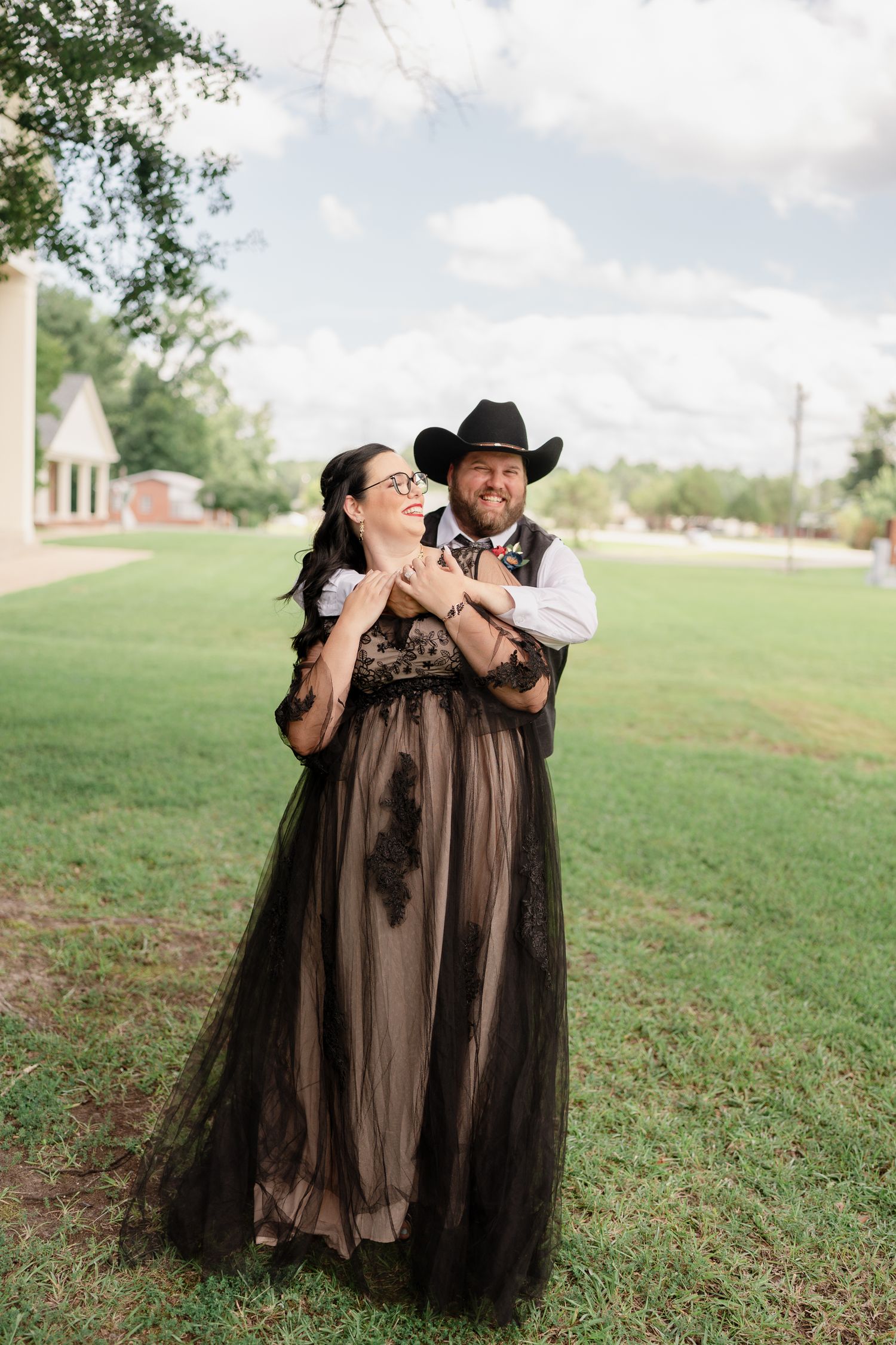 A series of romantic poses on a grassy lawn with a black tulle dress and western style attire.
