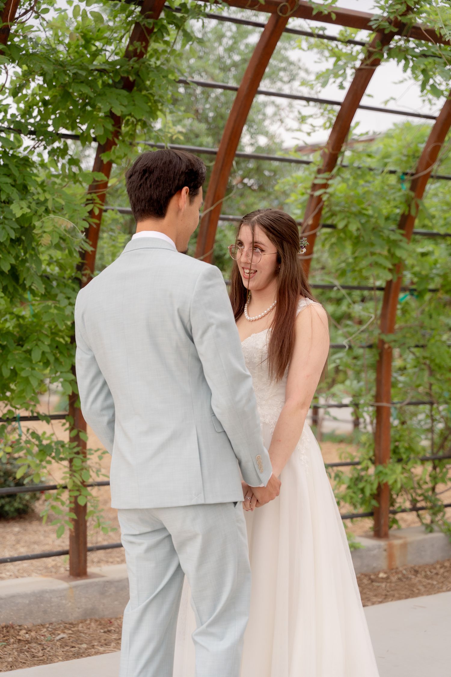Couple shares a joyful moment under a wooden pergola covered in greenery.