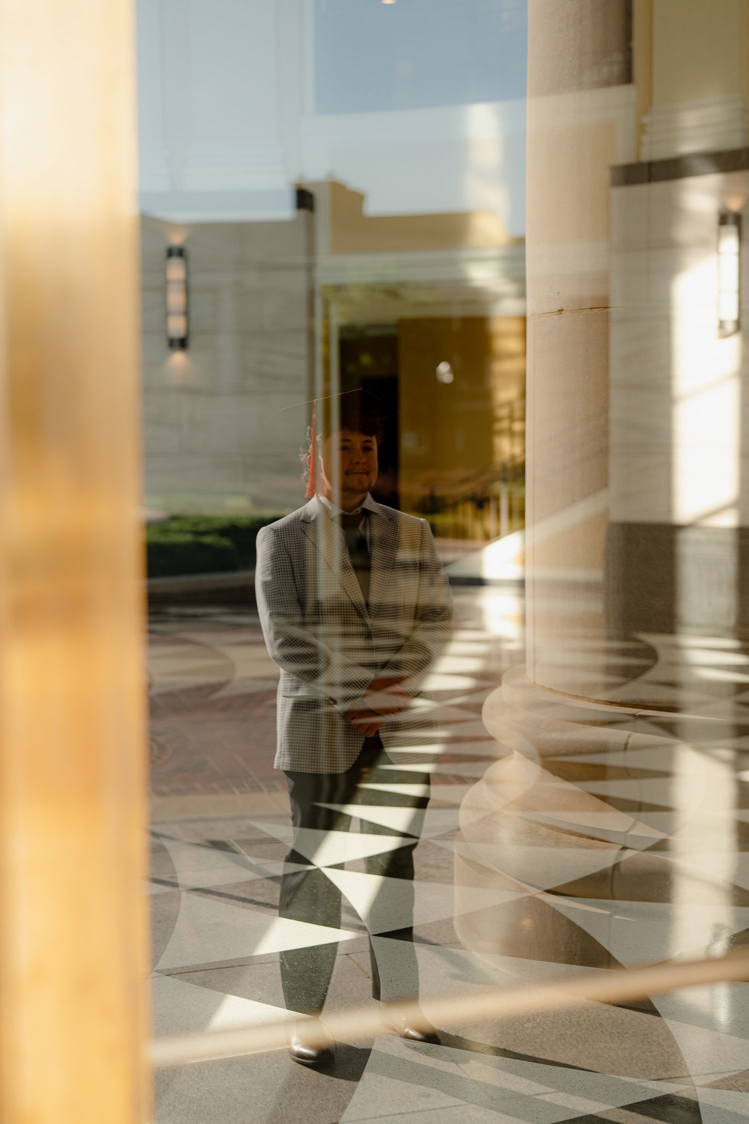 Man in gray suit reflected in glass building exterior with geometric light patterns on marble floor.