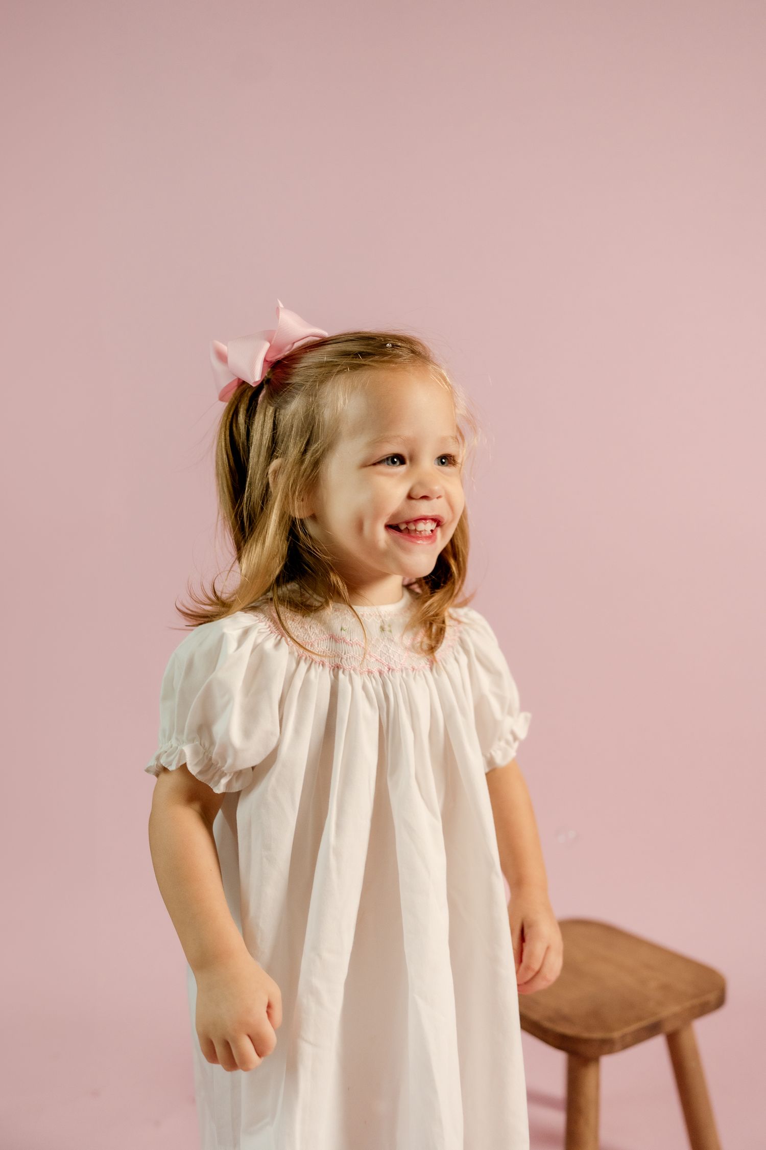 A candid moment of childhood happiness captured against a pink studio backdrop.