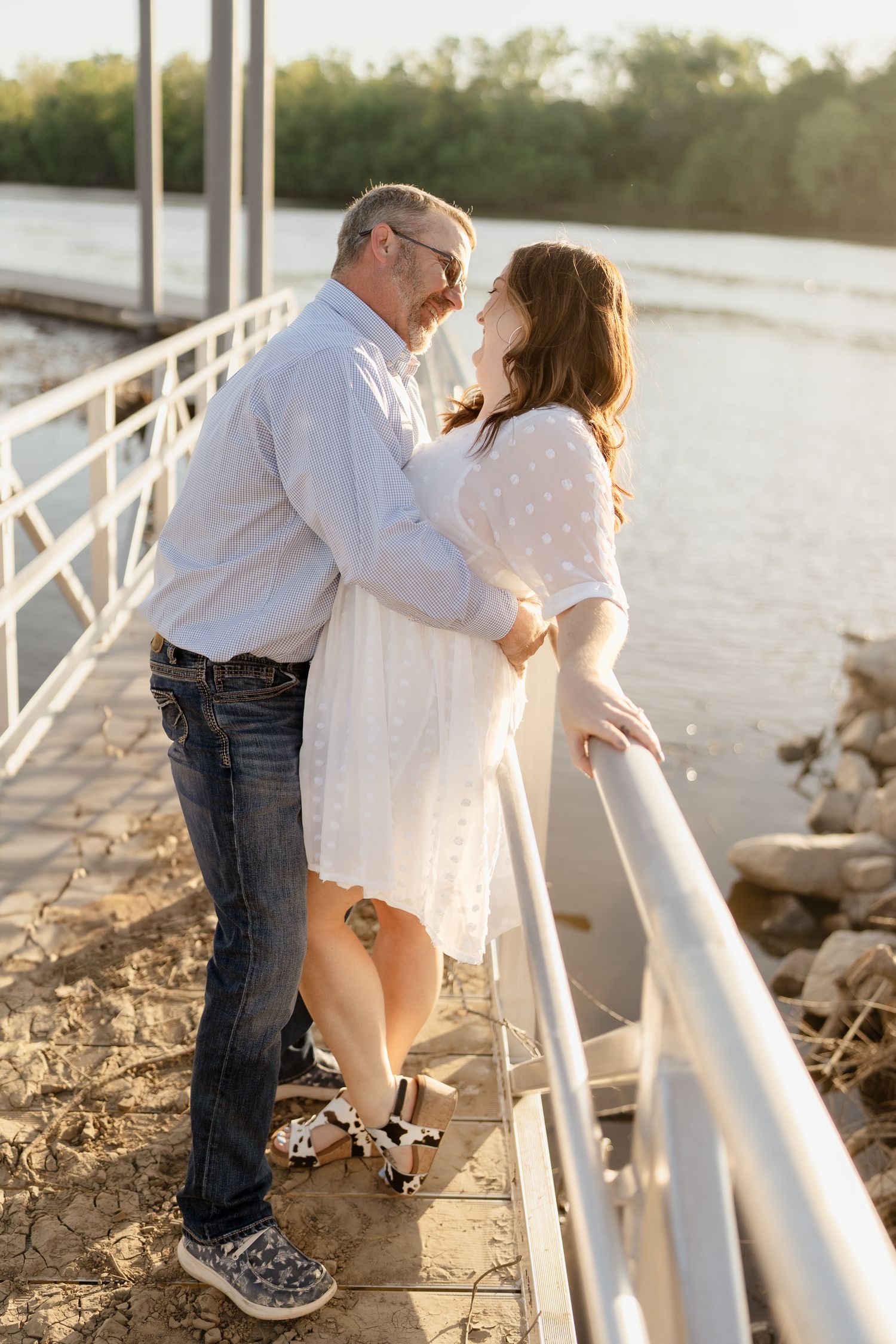 Two people share an intimate moment against a railing on a waterfront pier.