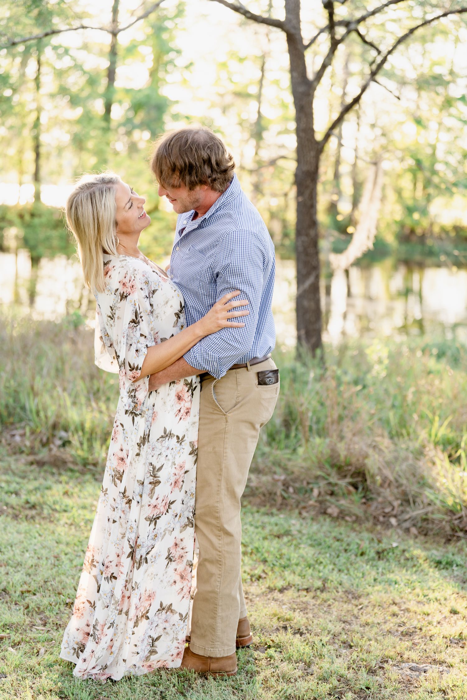 Romantic embrace between a couple in a floral dress and blue shirt against a wooded backdrop.