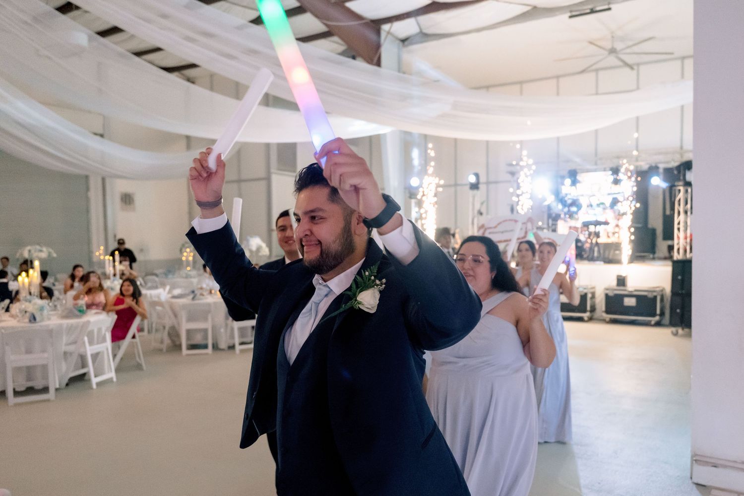 Guests dancing at an elegant white-decorated wedding reception venue with hanging lights and decorations.