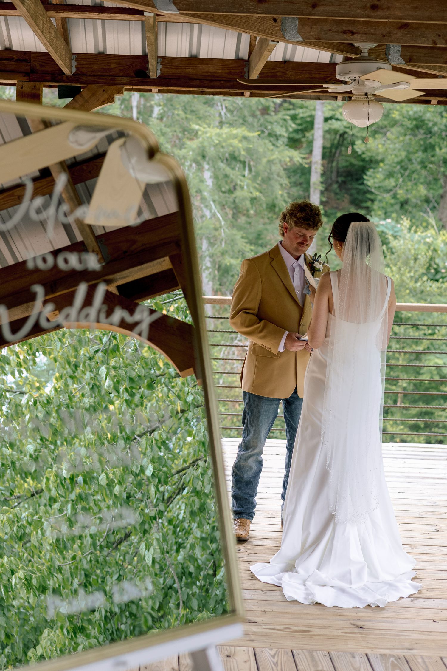 Bride and groom share an intimate moment on a wooden deck with lush greenery behind them.