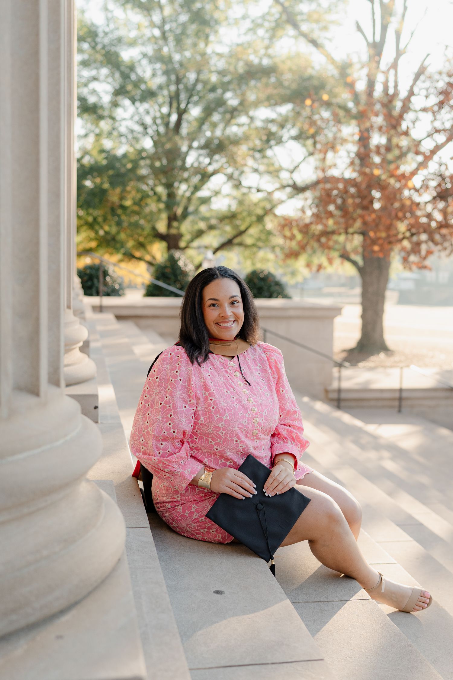 A person in a pink lace dress poses gracefully on stone steps during a sunny outdoor photo session.