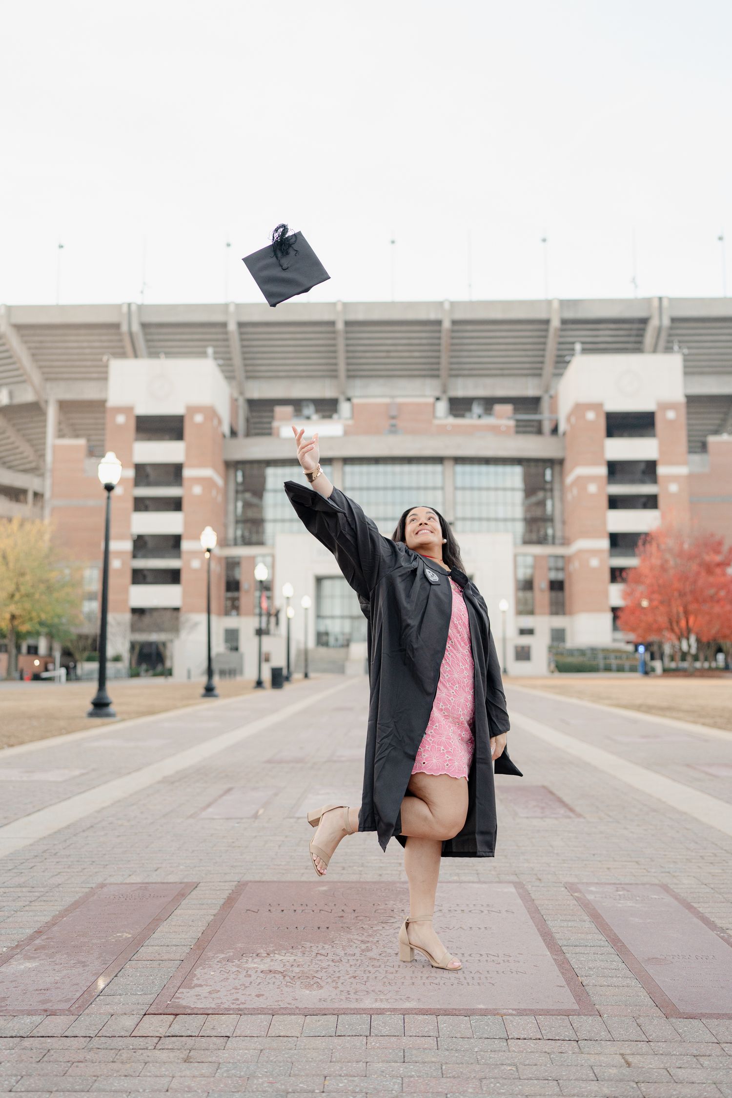 Dancing graduation photos captured in front of a stadium with pink dress and black graduation gown.