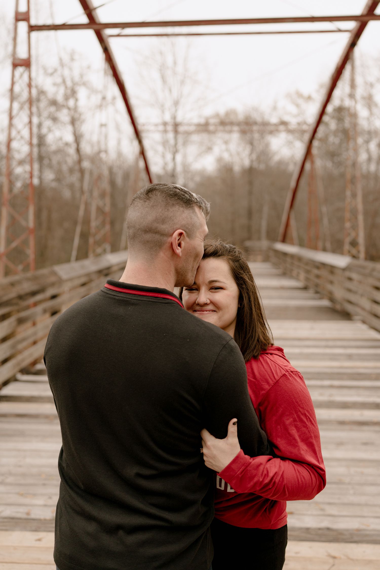 A romantic couple embraces on a rustic wooden bridge during an outdoor photoshoot.