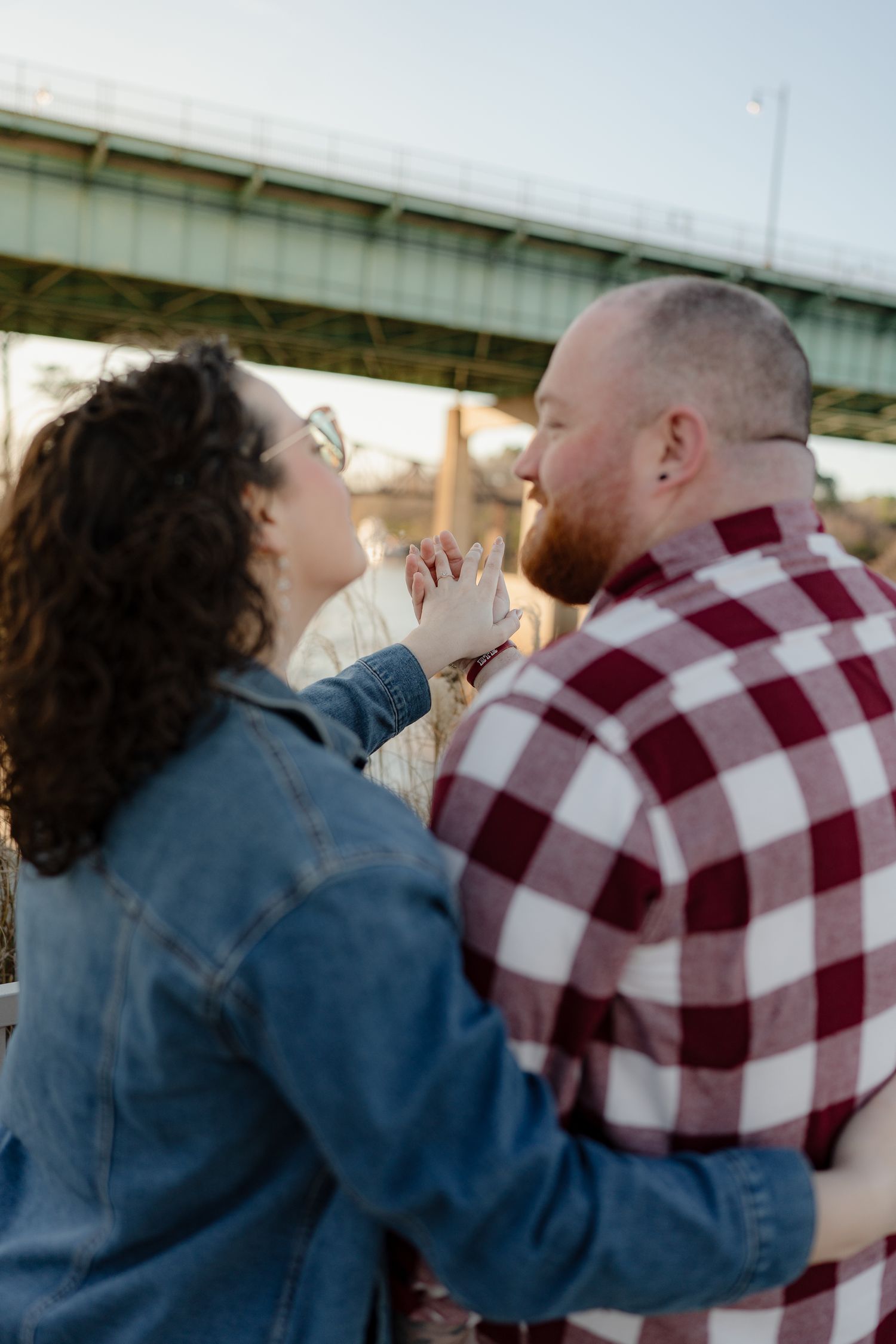 Two people share an intimate dance moment beneath a bridge structure at sunset.
