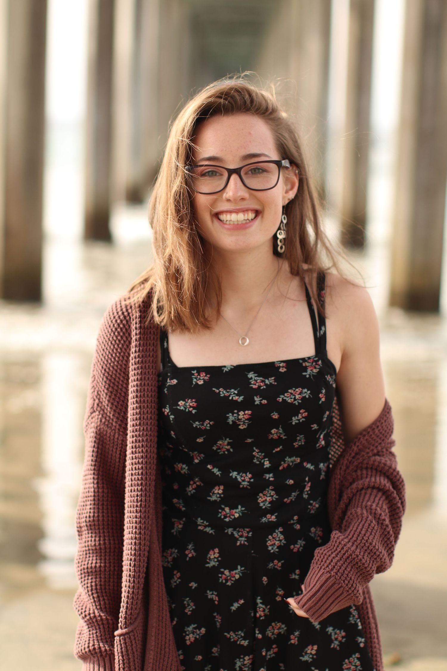 Portrait under columns wearing floral dress and mauve cardigan.