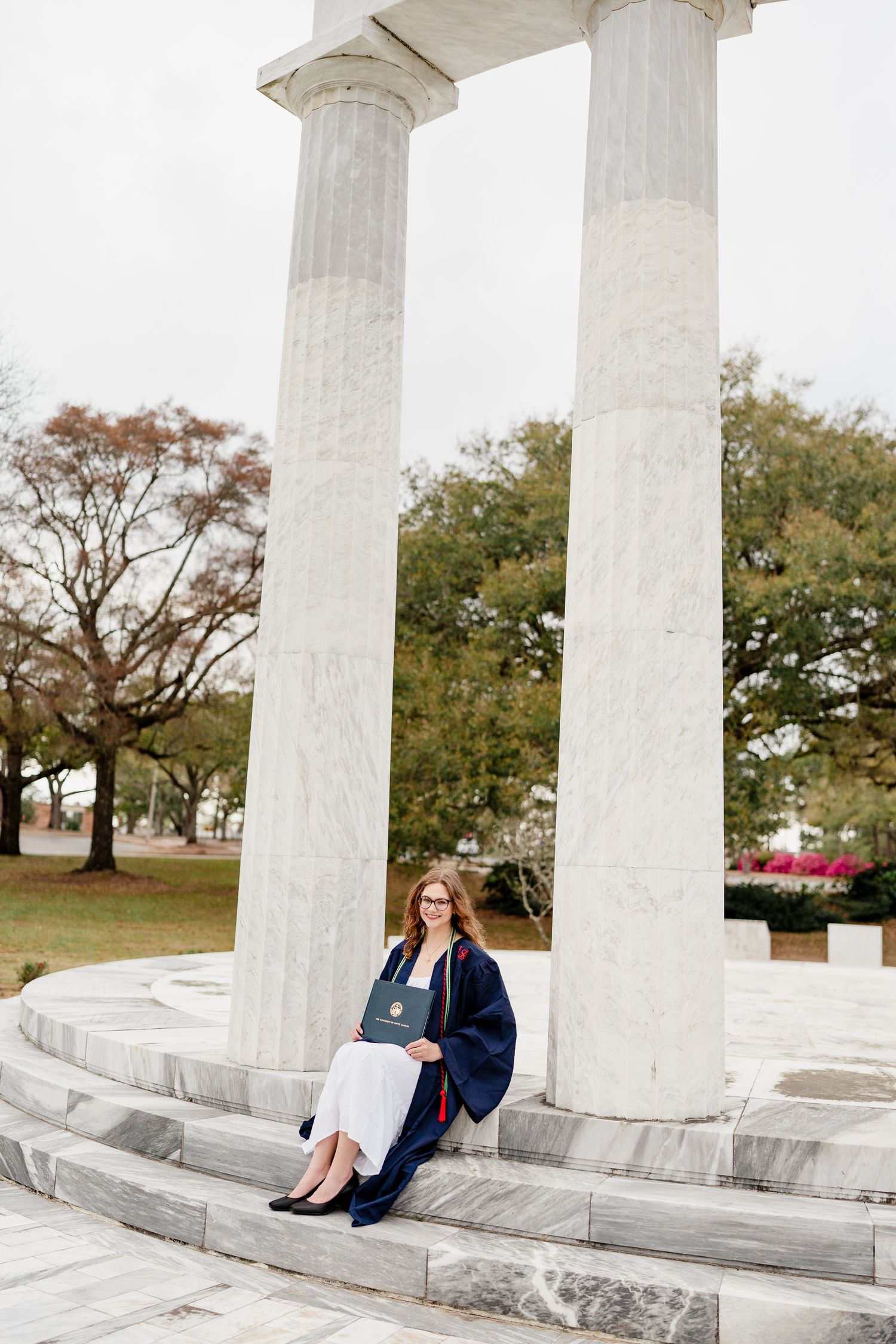 Graduate lounges on marble steps between majestic white columns during photo shoot.