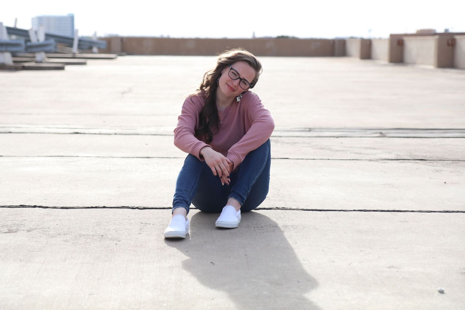 Casual portrait of woman in pink top sitting on concrete surface outdoors.