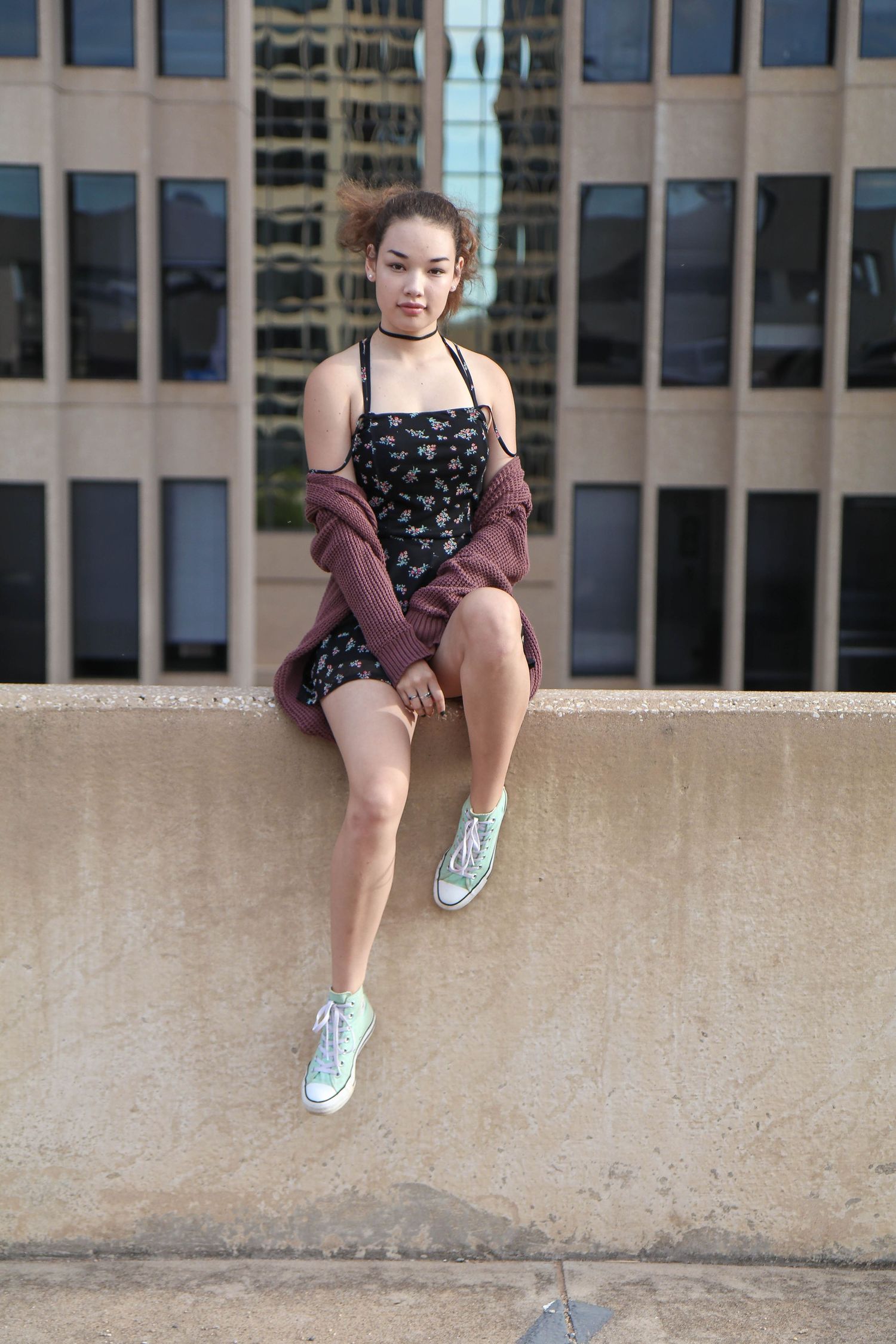 Person sitting casually on concrete ledge outside office building.