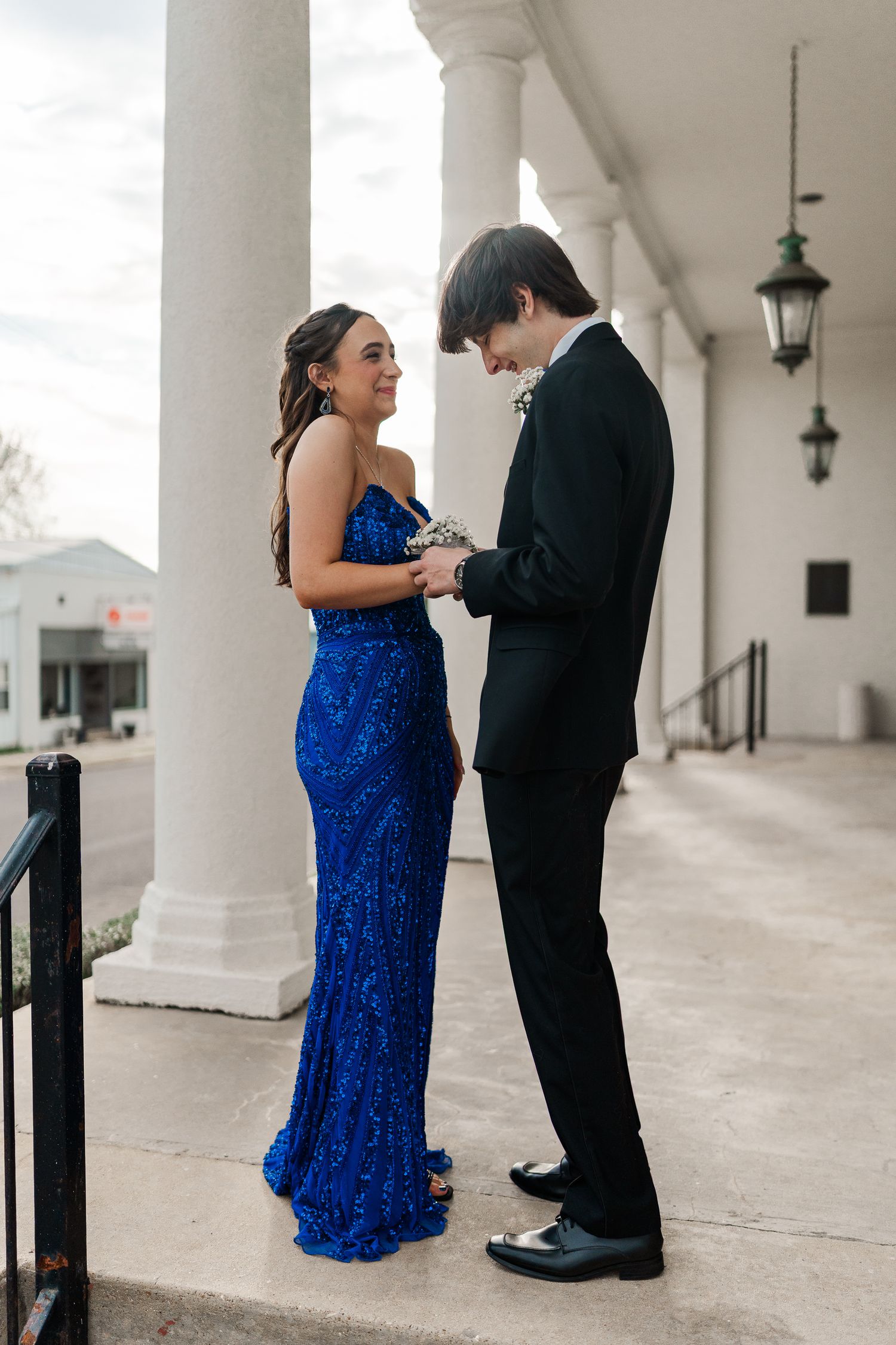 Couple in formal attire sharing an intimate moment under a colonnade with hanging lanterns.
