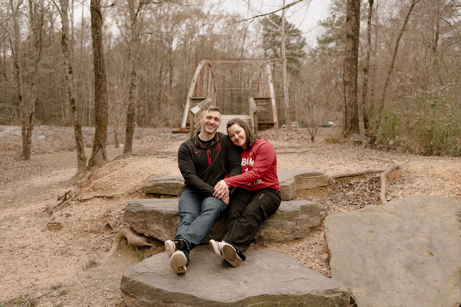 A couple sits together on concrete steps at a playground surrounded by bare trees.