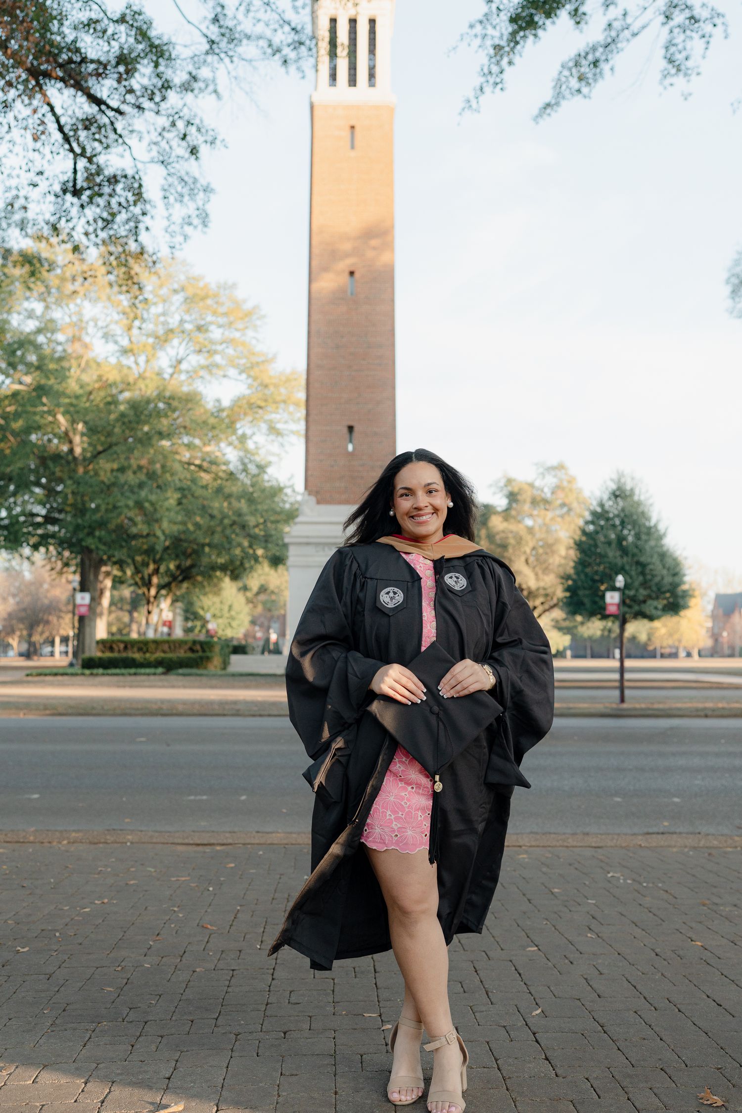 Graduation photos taken in front of a tall clock tower on a brick paved plaza during golden hour.