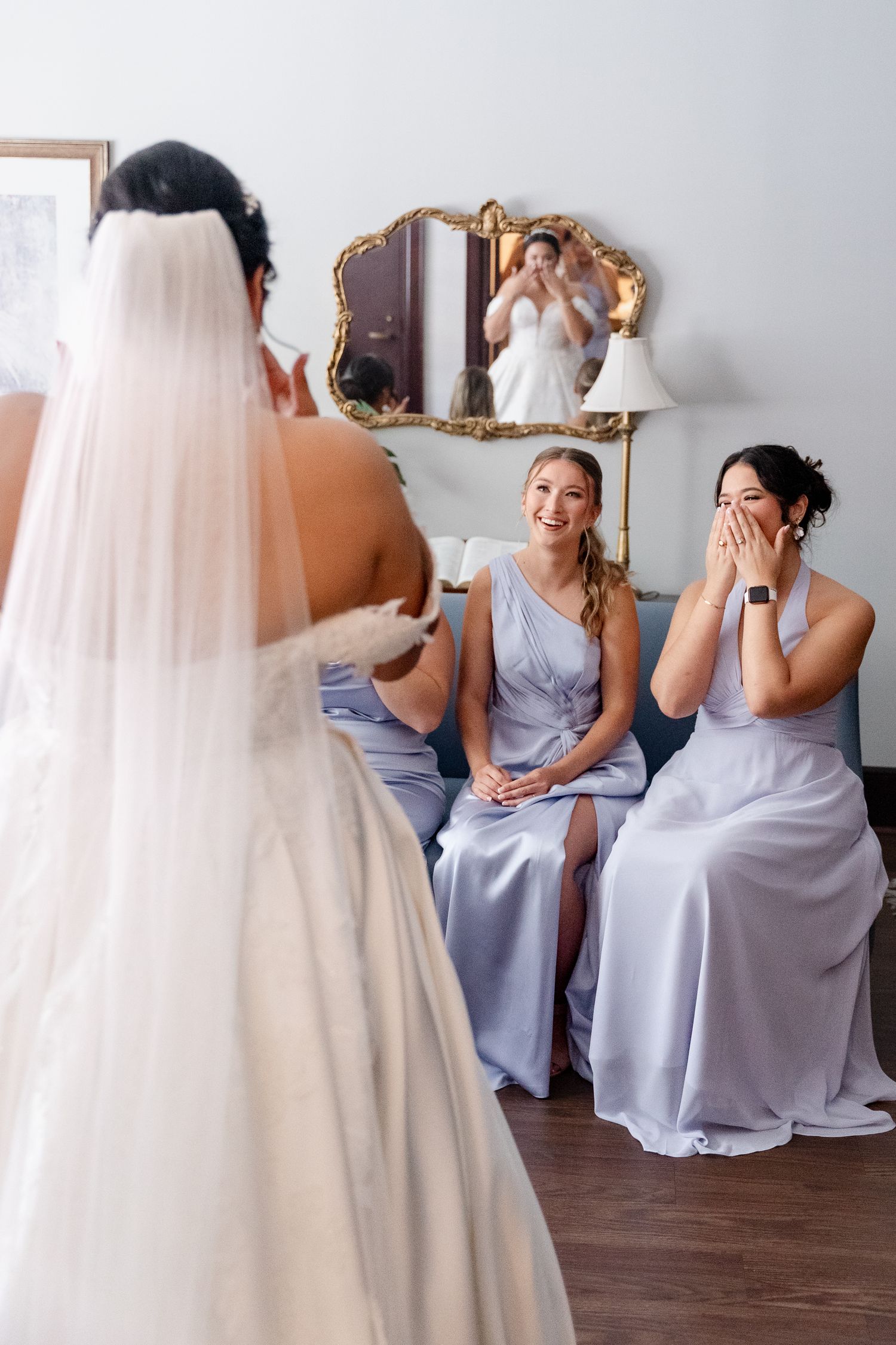 Bridesmaids in light blue dresses react emotionally to seeing bride in white wedding gown for first time.
