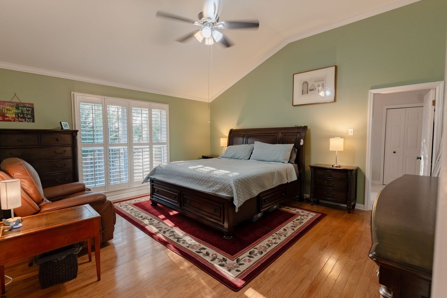 Spacious bedroom with hardwood floors, sage green walls, and large windows showcasing natural light.