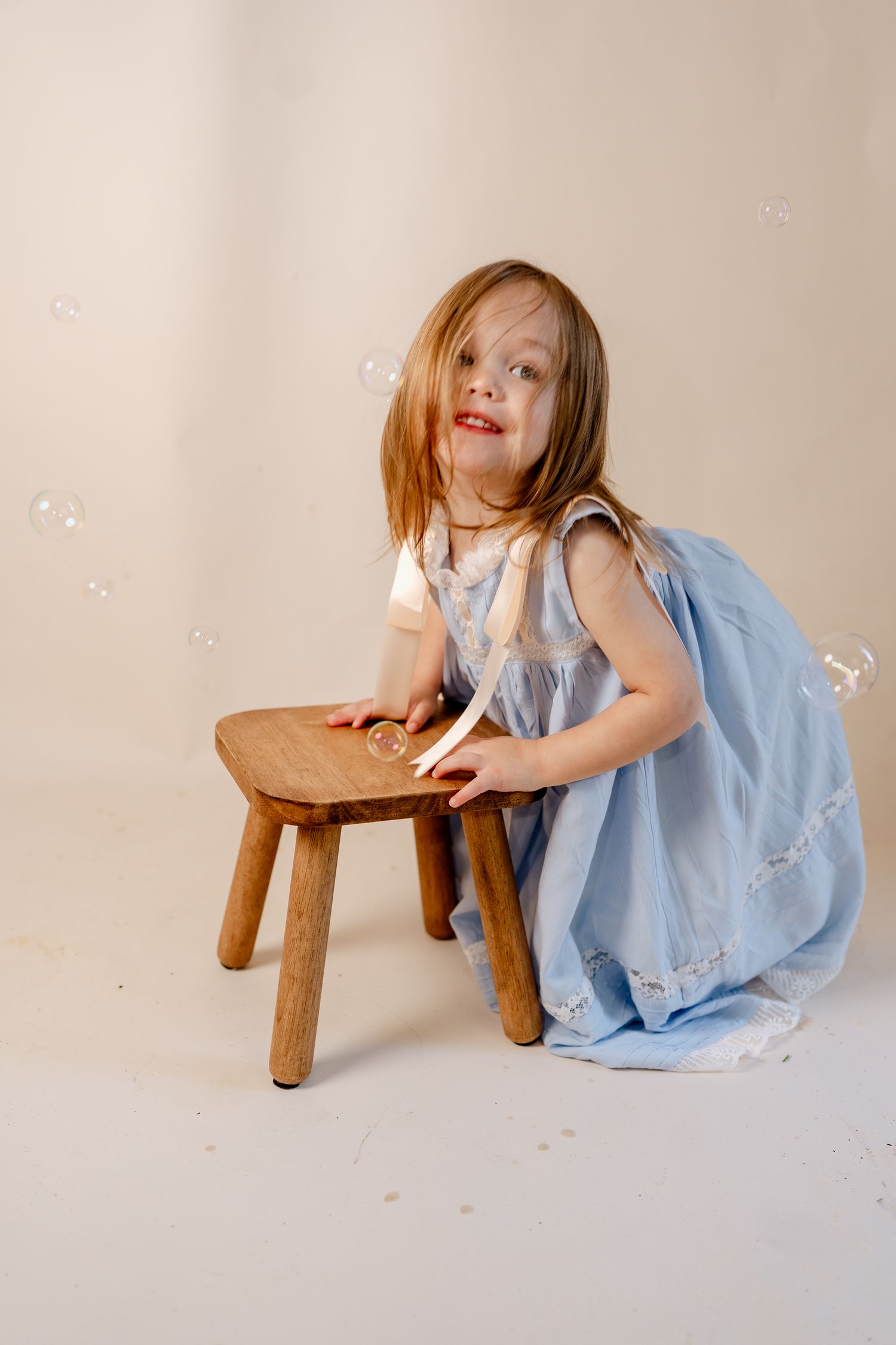 A rustic wooden stool is paired with a light blue dress in a minimalist studio setting.