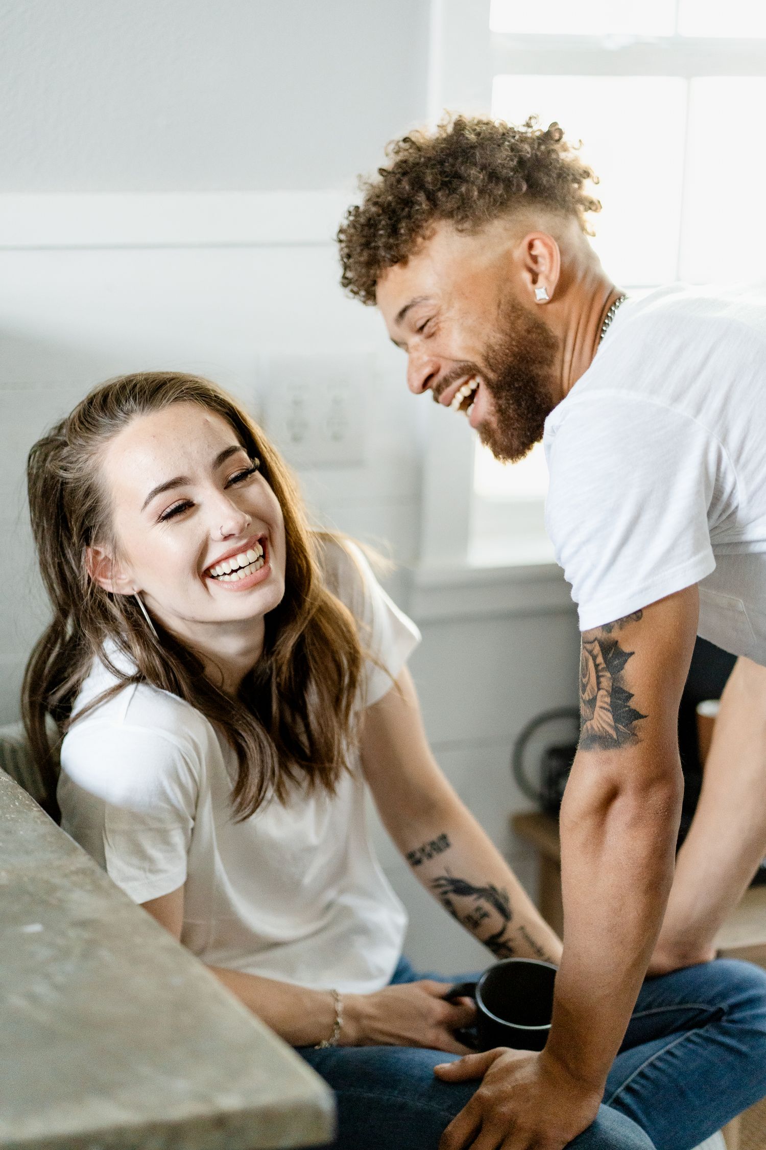 Candid moment of couple laughing together in bright modern kitchen setting.