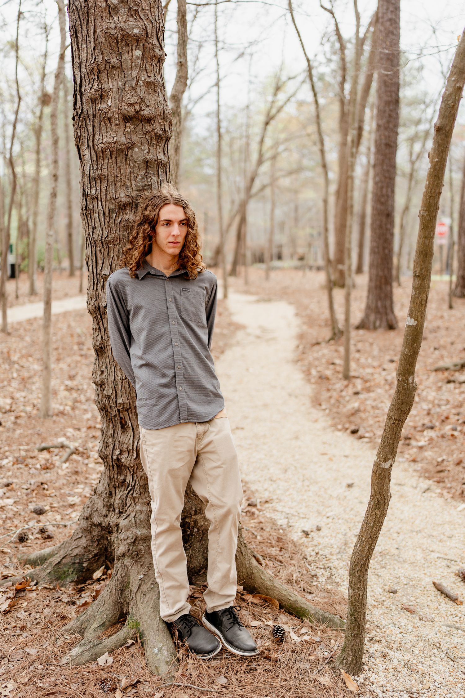 Person in gray shirt and khakis posing against trees on a forest trail.