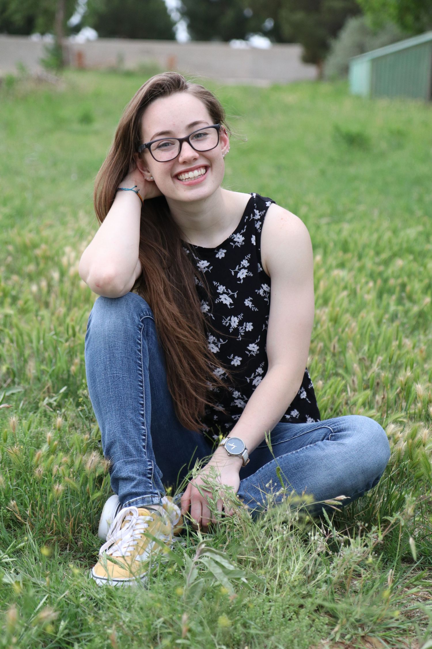 A stylish casual outfit featuring a floral sleeveless top and jeans while sitting in grass.