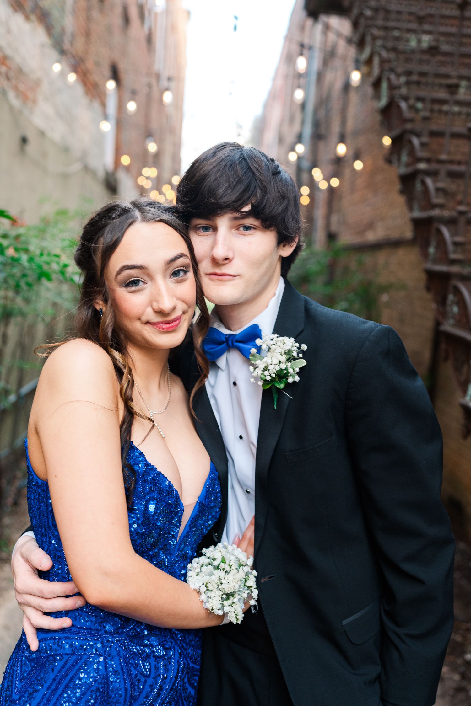 A couple poses for formal photos wearing a sparkly blue dress and black tuxedo with baby's breath flowers.
