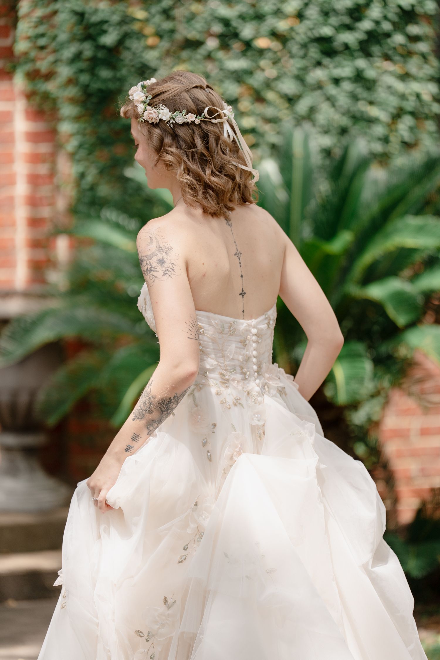 A bride in a flowing white wedding dress spins around in a garden setting with brick walls and greenery in the background.