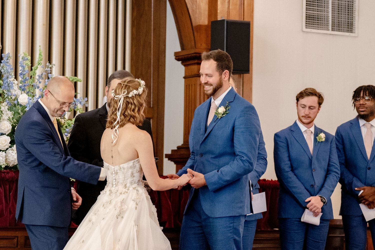 Wedding ceremony in progress with bridal party and guests in traditional church setting.