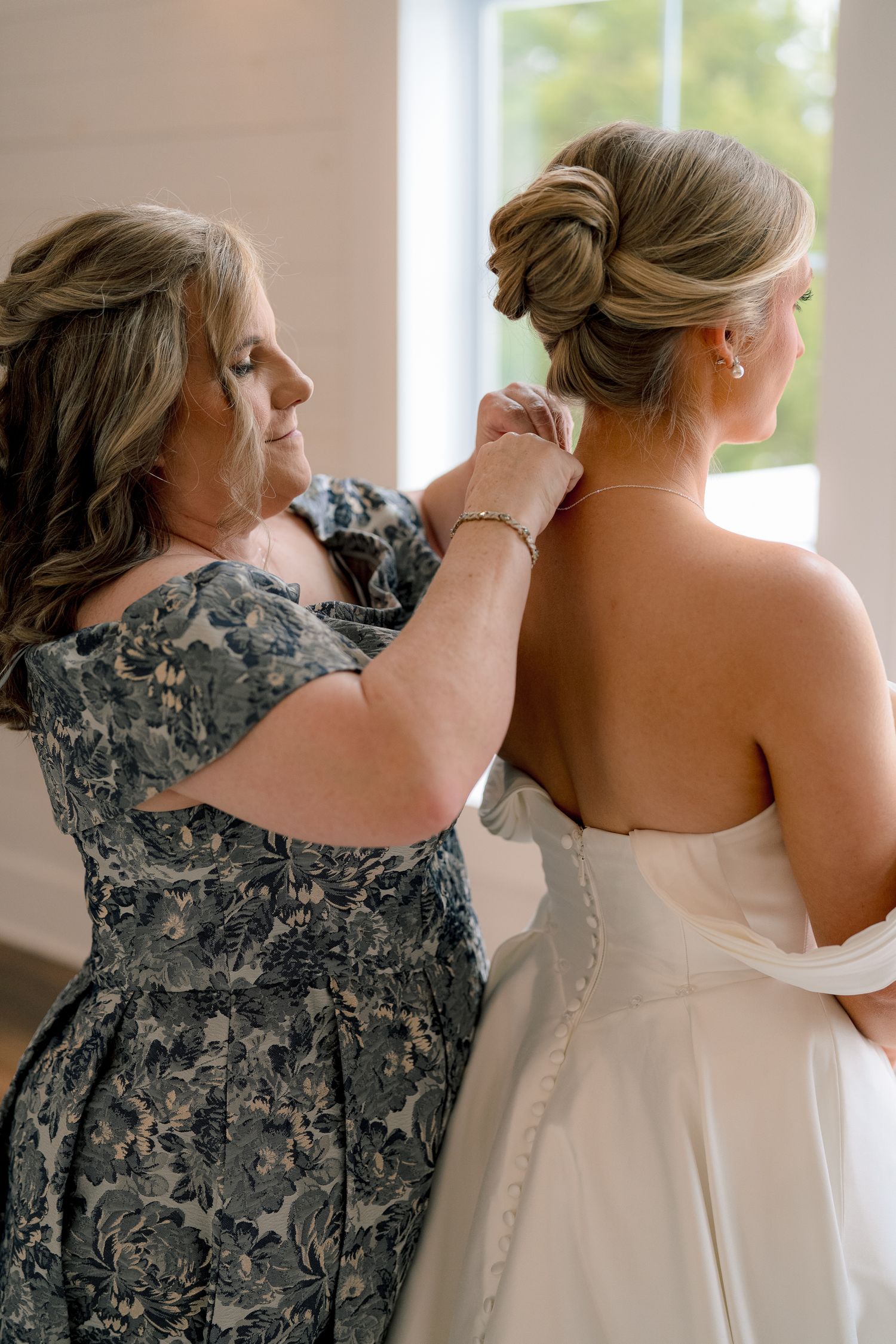 Mother helping bride button her elegant white wedding gown before the ceremony.