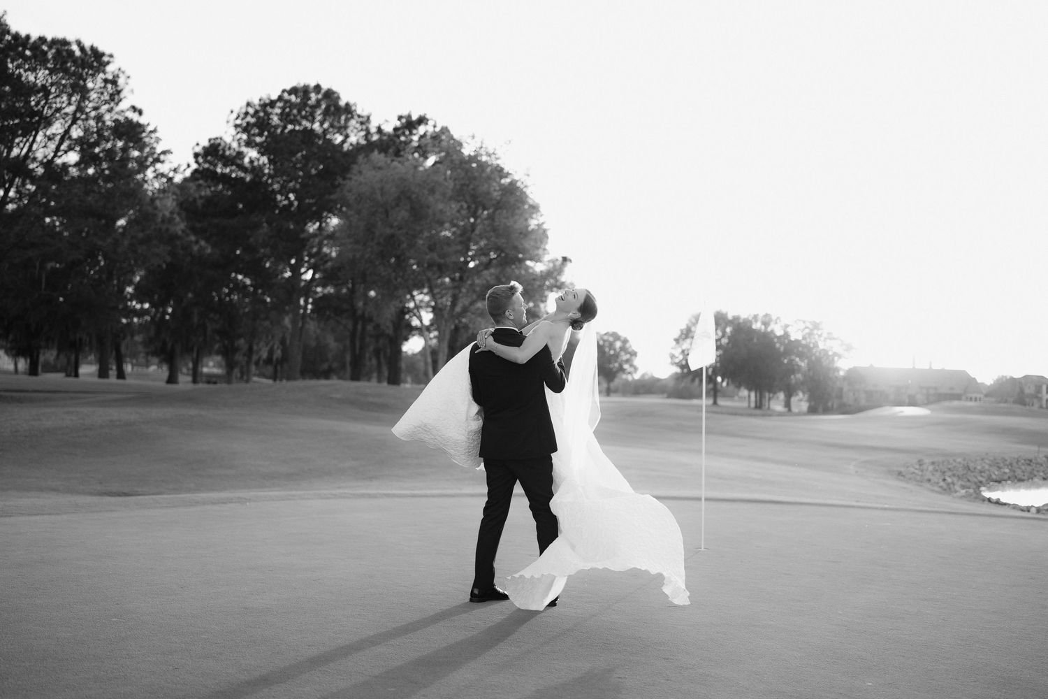 Black and white photo of bride and groom sharing a romantic dip kiss on a golf course wedding venue.