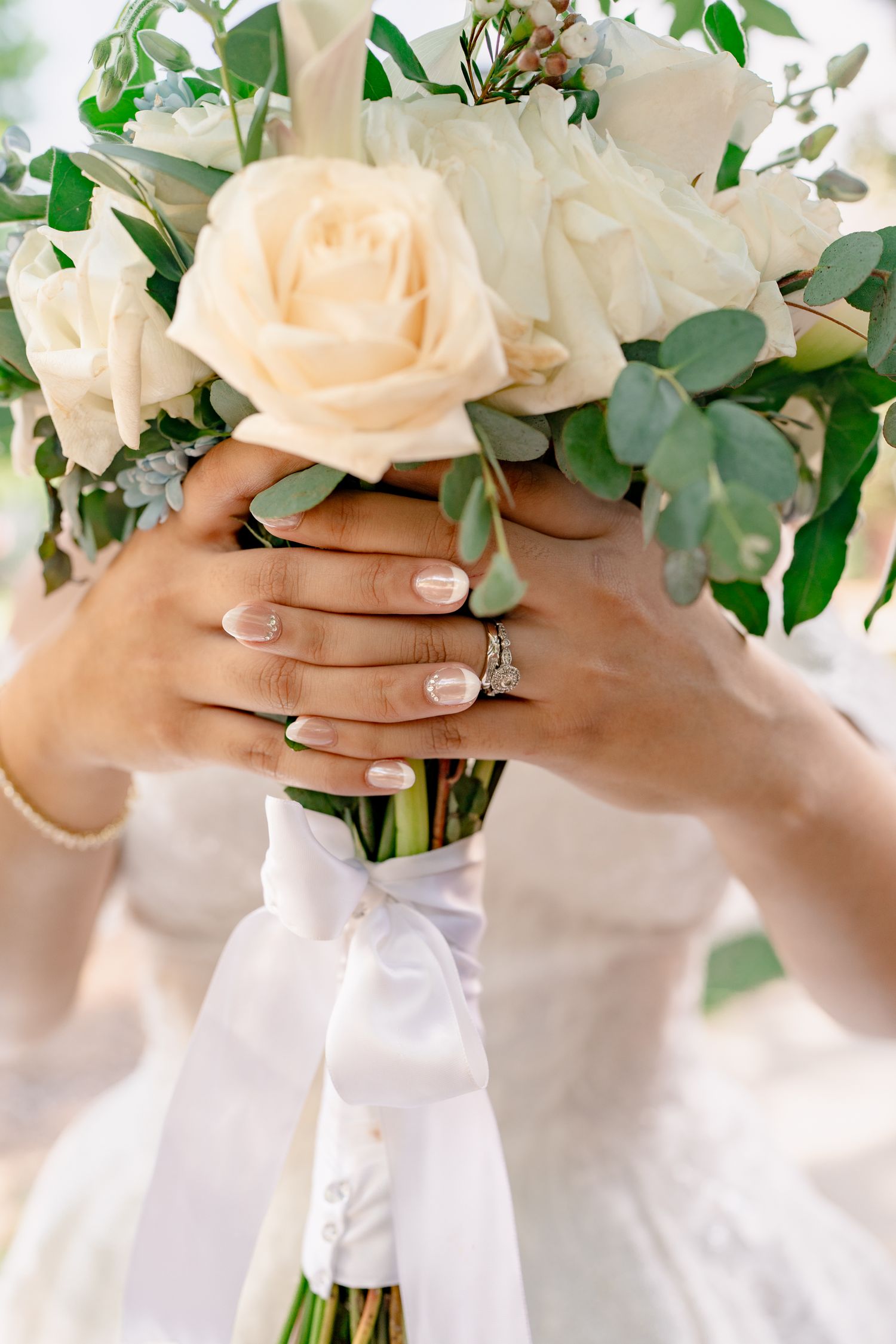 Close-up of hands holding a romantic blush rose wedding bouquet with eucalyptus accents.
