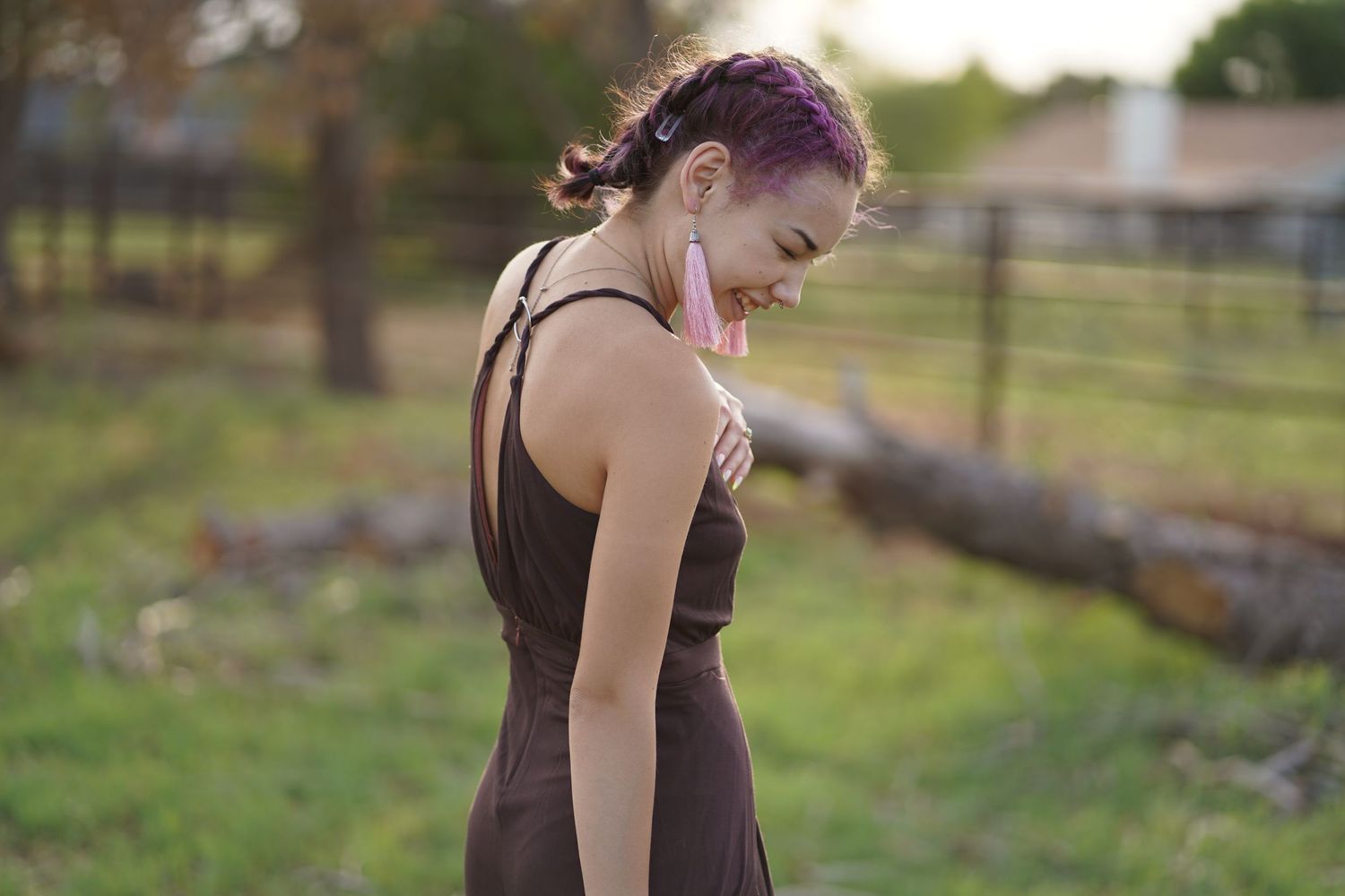 Person with purple hair in dark dress looking down in garden setting.