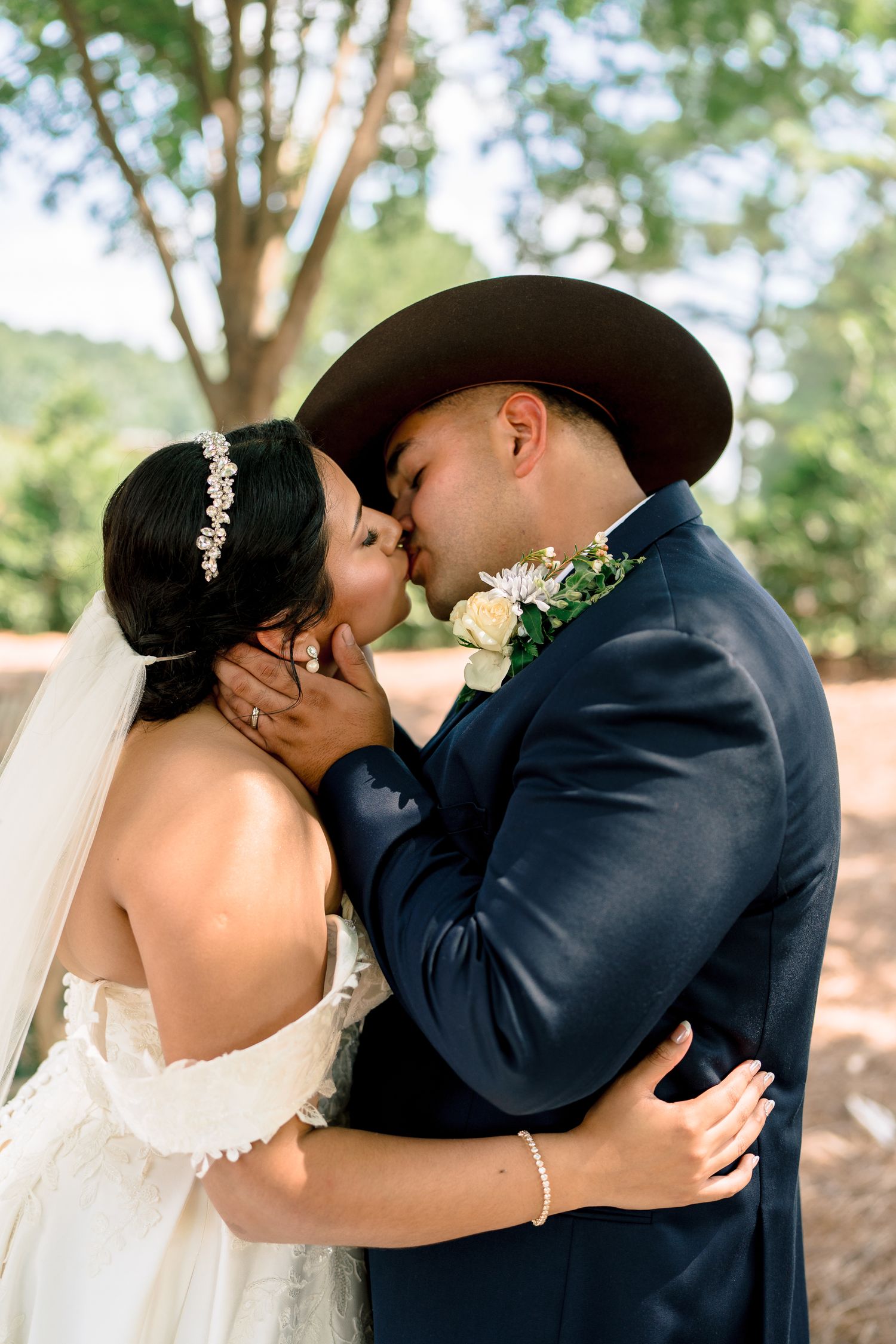 A romantic wedding kiss between newlyweds with the bride in white and groom in black cowboy hat.