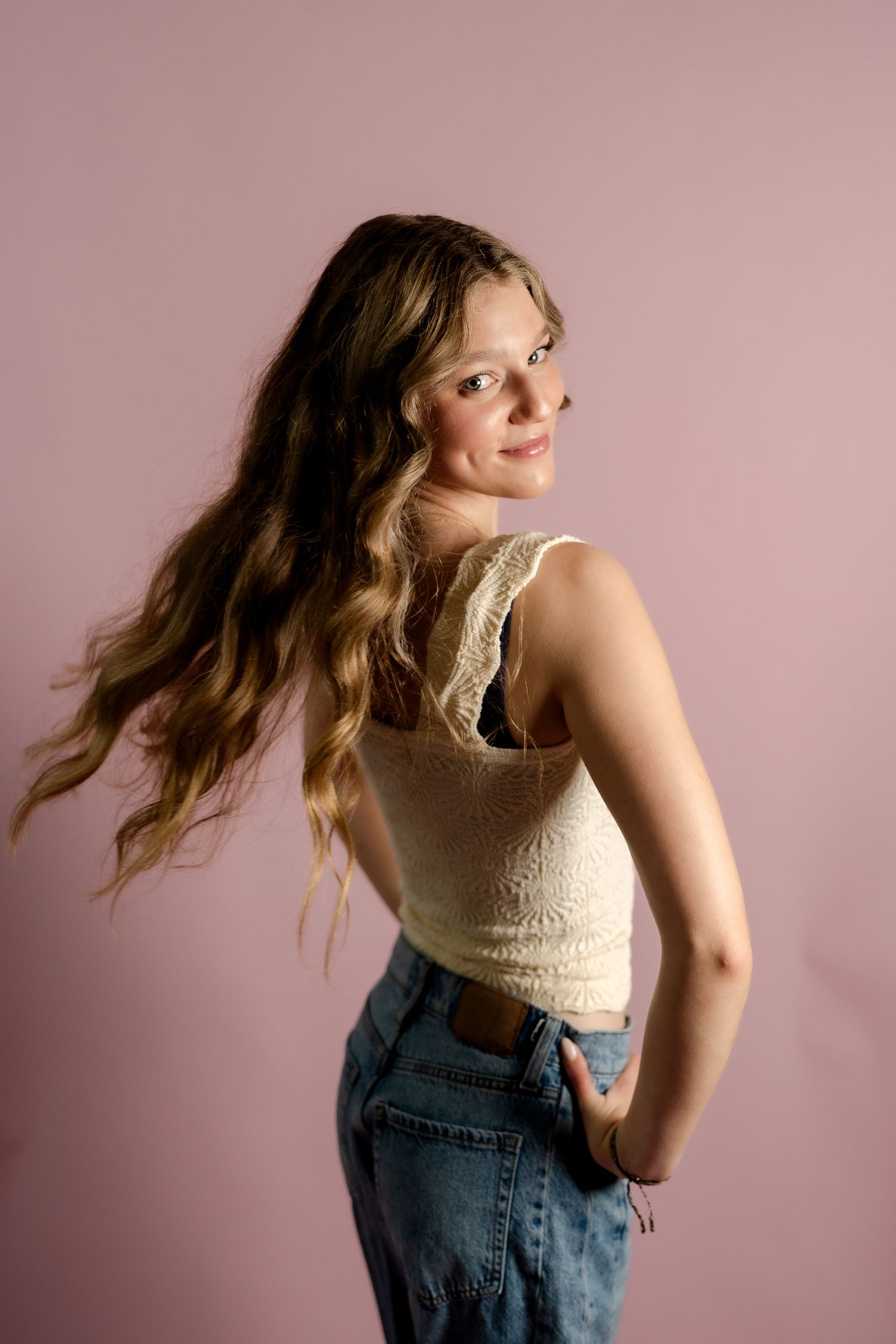 Profile shot showcasing wavy hair and vintage-inspired casual outfit against pink backdrop.