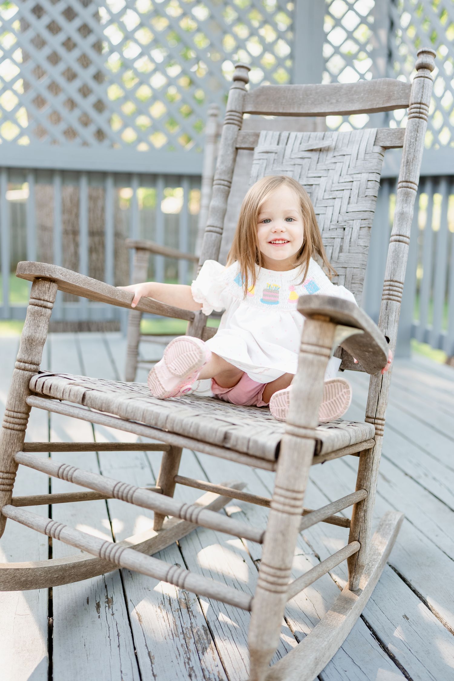 Wooden rocking chair on a rustic porch with lattice background.