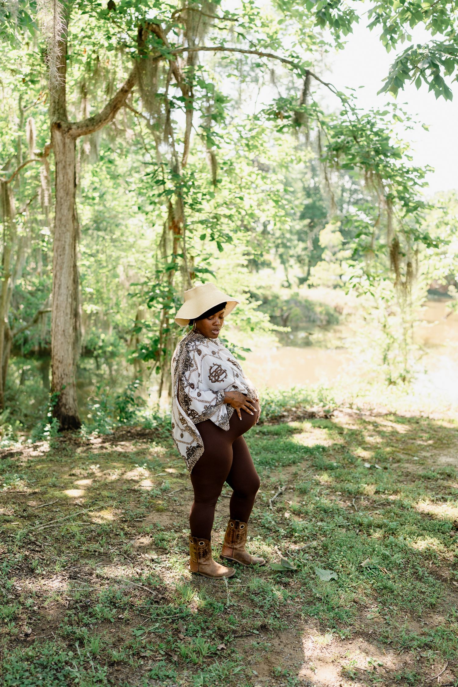 Person in patterned dress and sun hat standing in a serene wooded area.