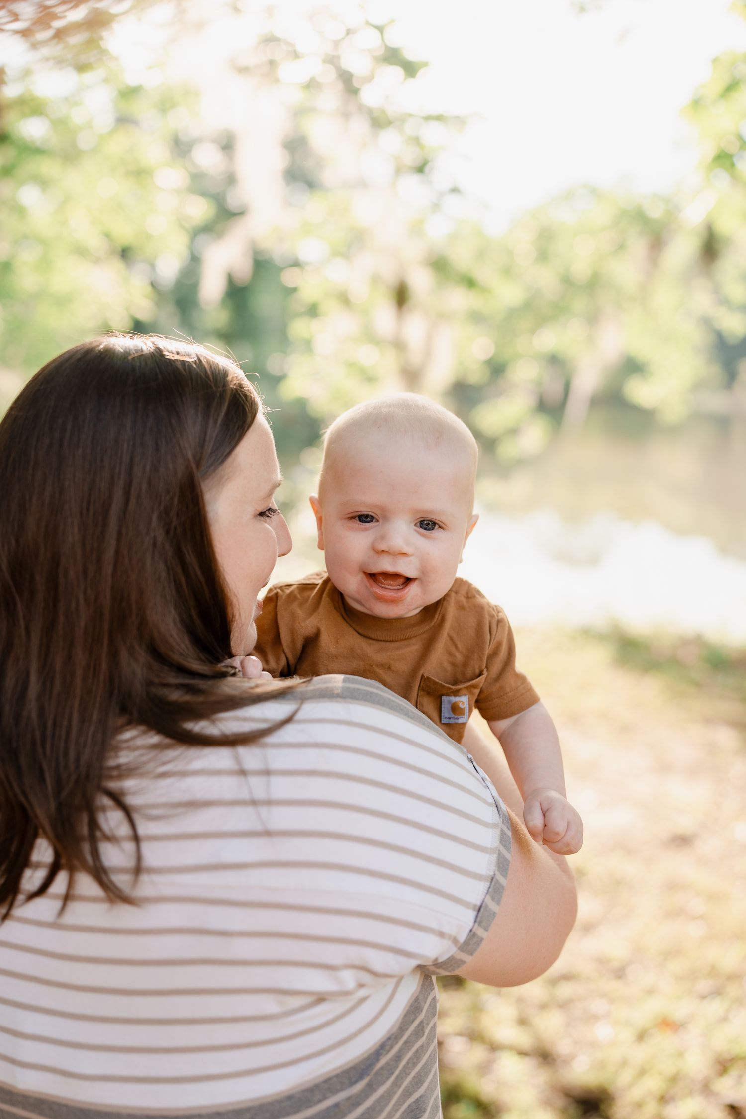 Mother and baby share joyful moments outdoors in dappled sunlight.