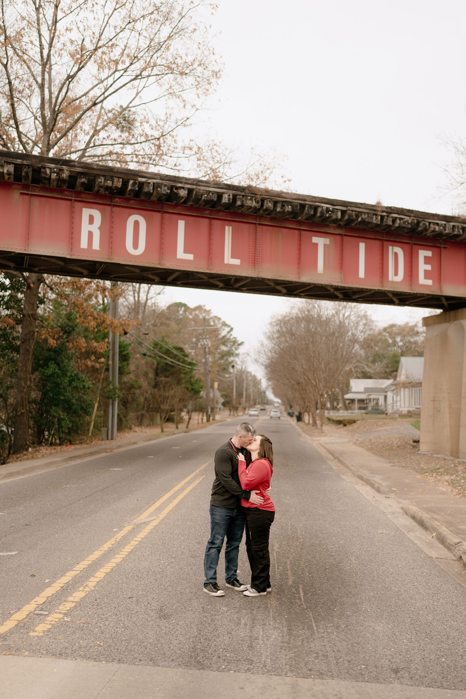 A couple stands beneath a red railroad bridge on an empty street.