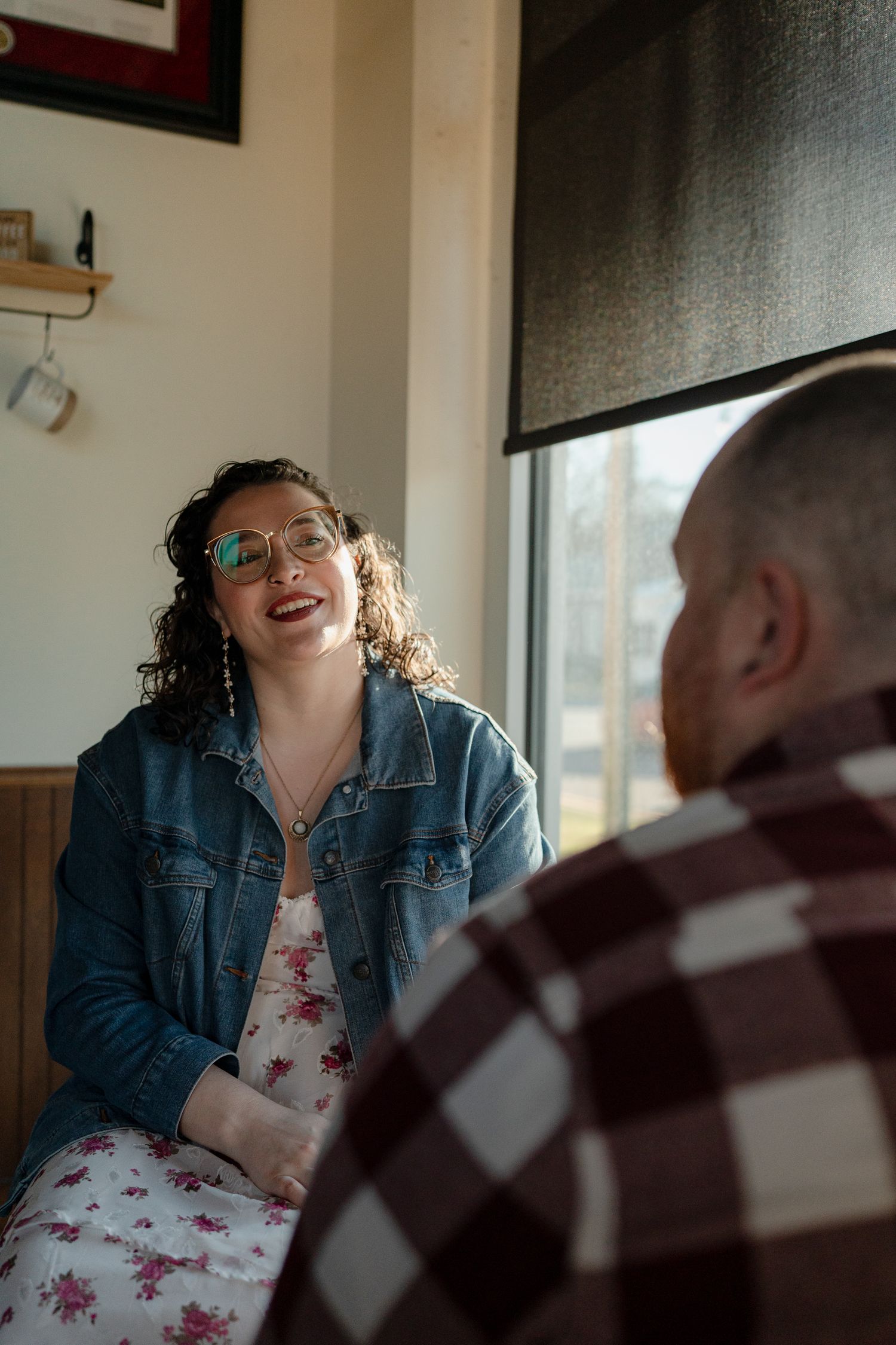 A couple shares a joyful moment indoors, with one wearing a denim jacket and floral dress.