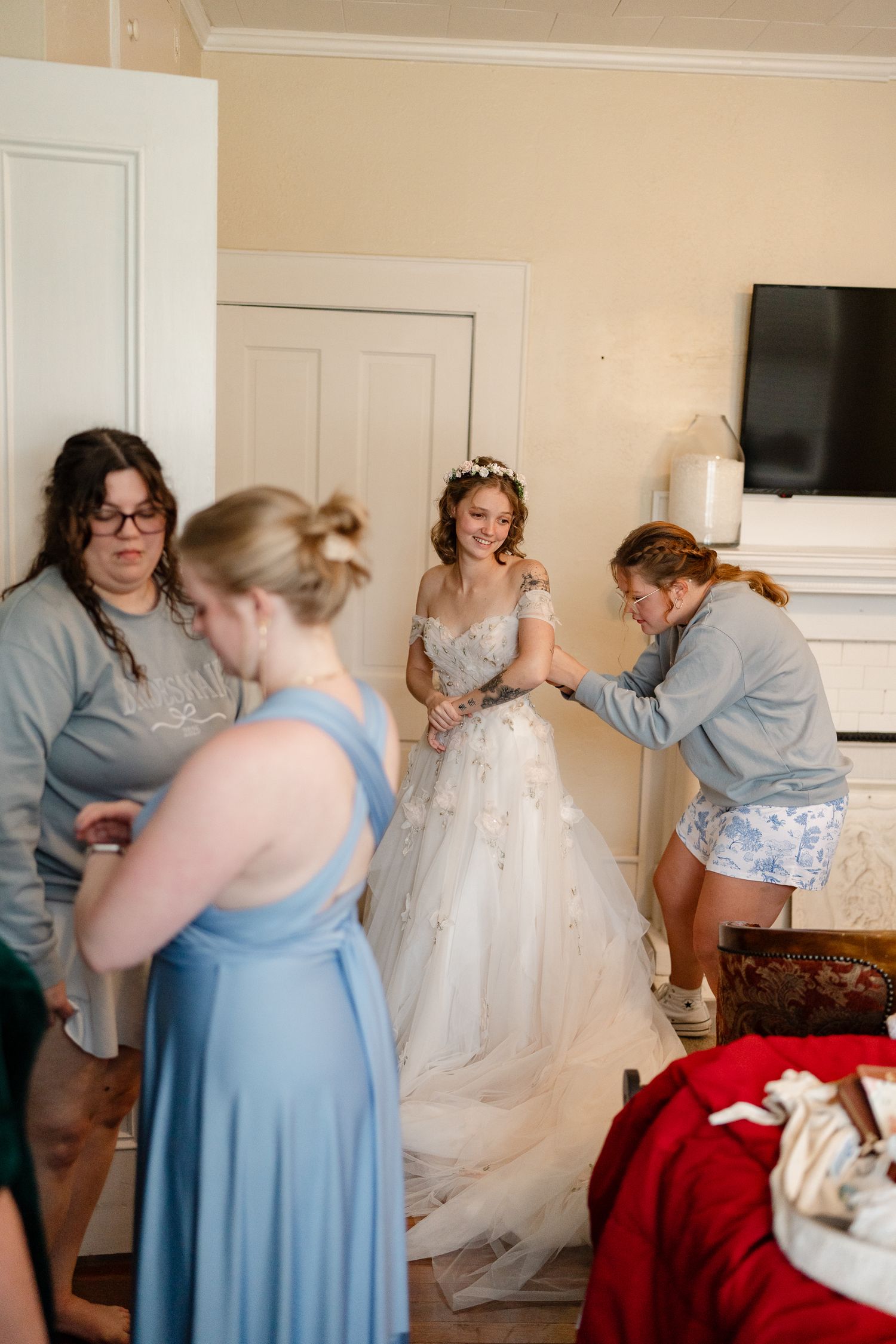 Wedding preparation scene showing bridesmaids in light blue dresses helping with a white wedding gown.