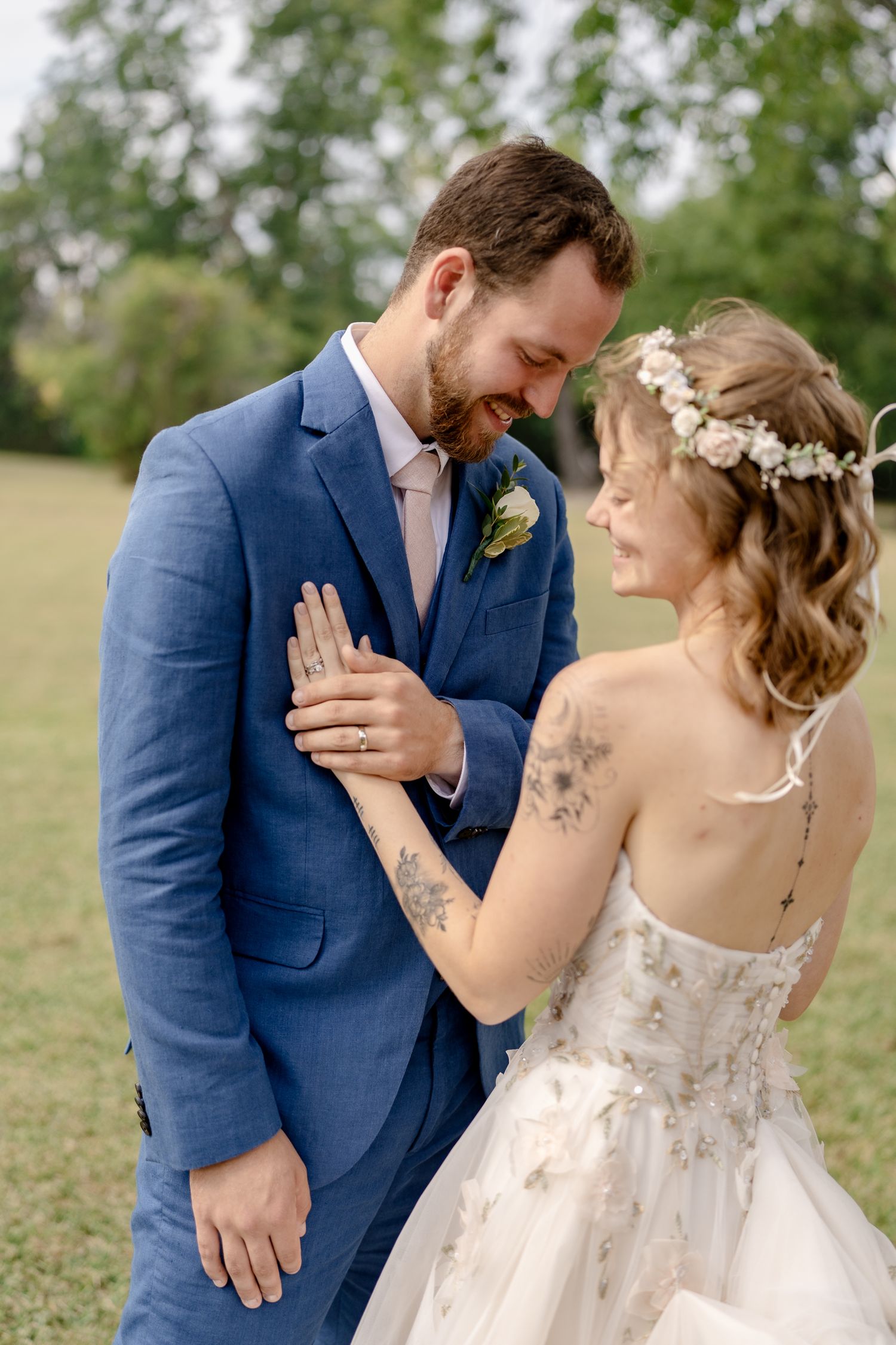 Emotional first look reaction between newlyweds in a garden setting with bride in lace gown and groom in blue suit.