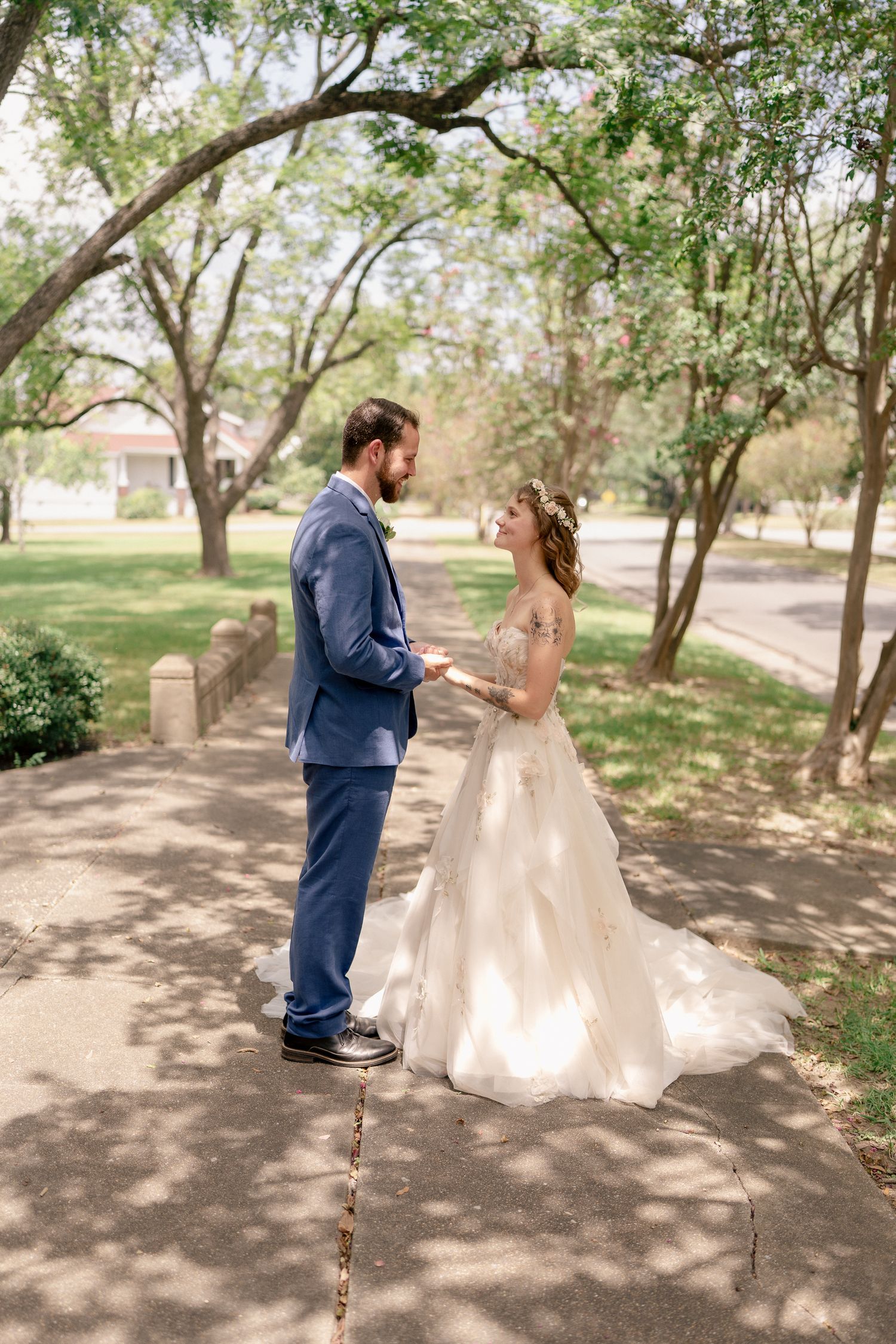 A wedding couple shares candid moments on a tree-lined path during their outdoor photo session.