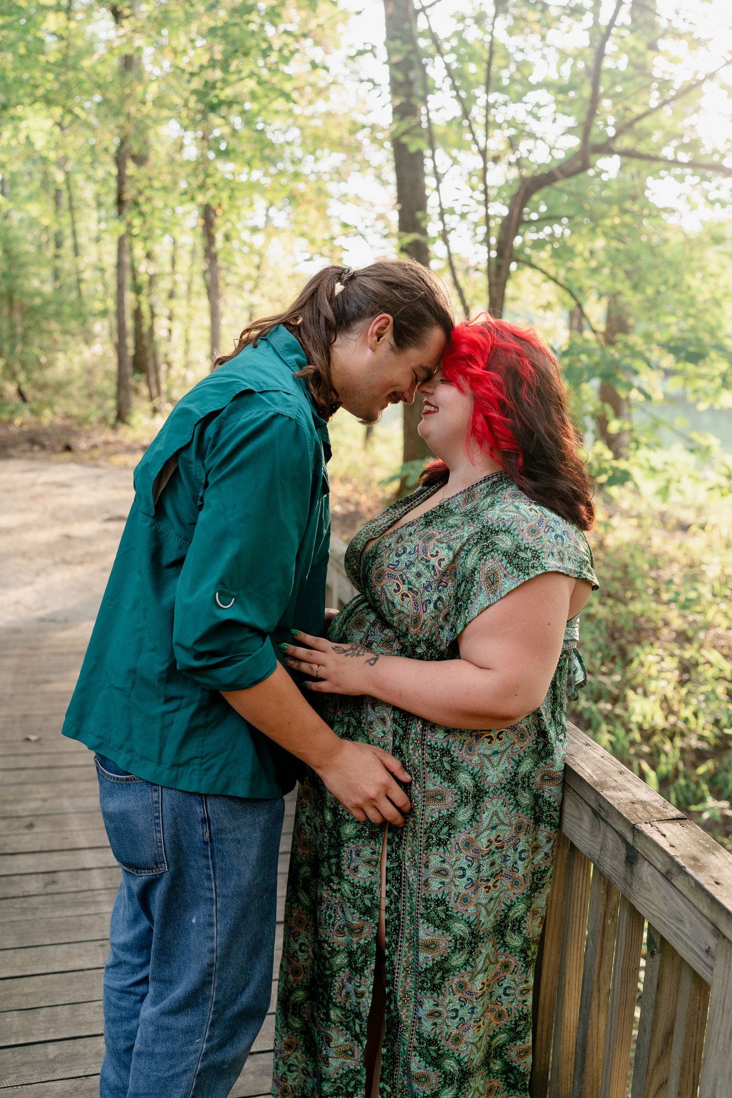 A couple shares an intimate moment on a wooden boardwalk surrounded by lush green forest.